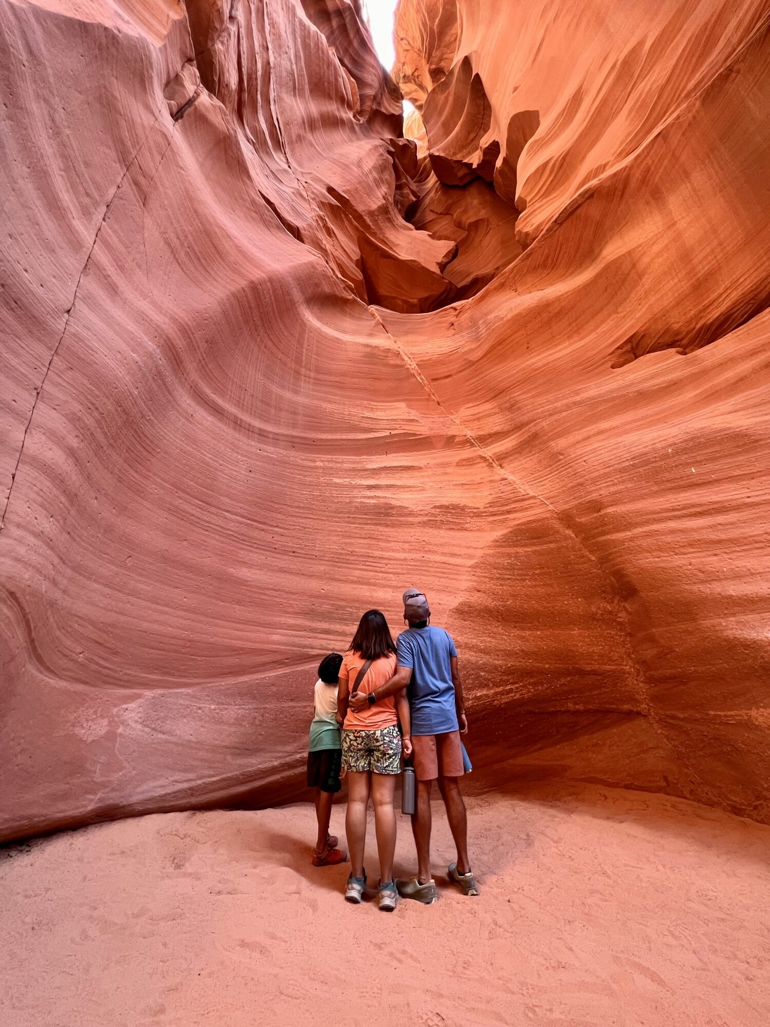 Family standing together inside a slot canyon of smooth, swirling orange sandstone