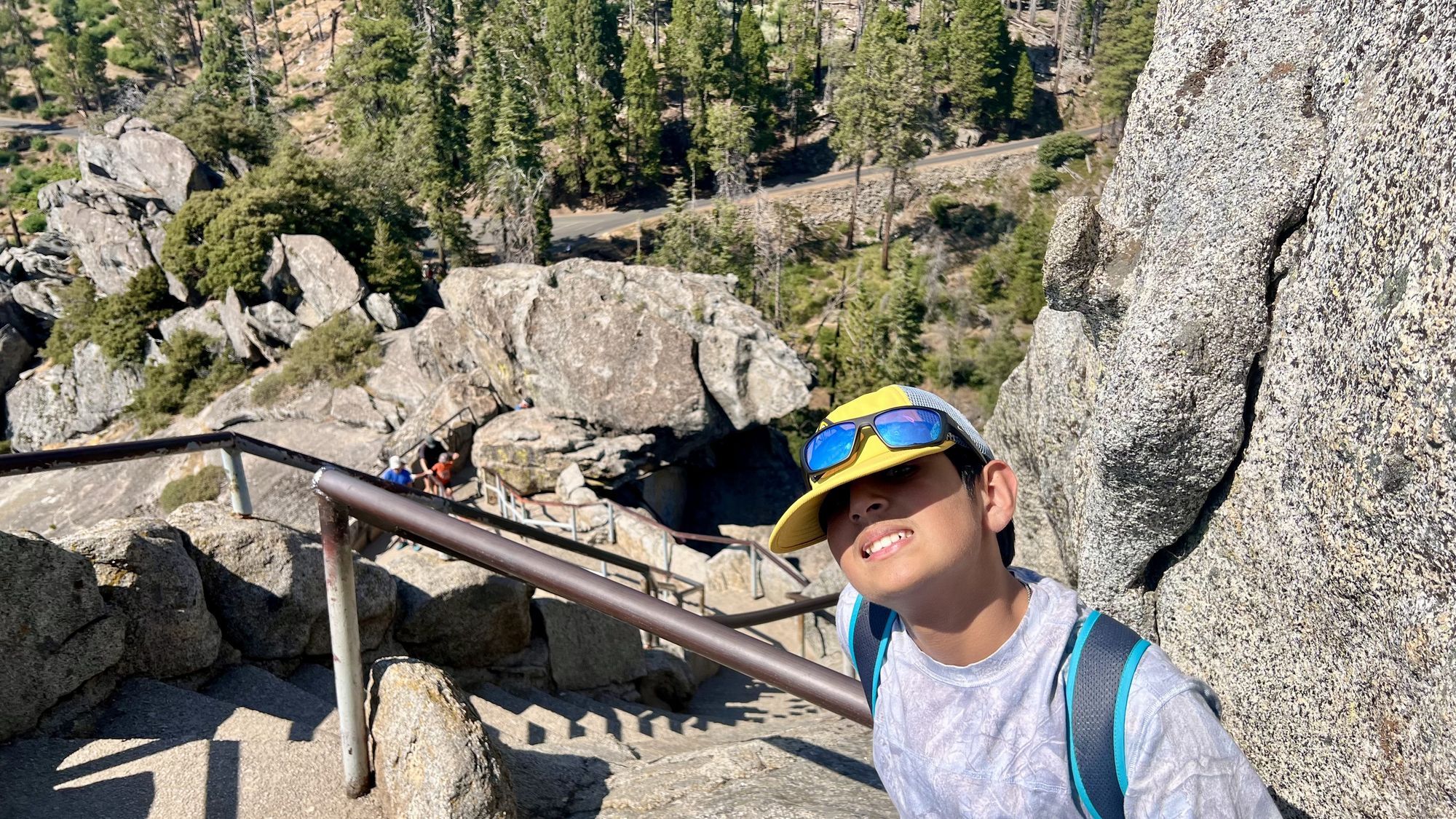 Our son smiling on the Moro Rock stairway, with a metal railing and a steep drop of granite and pines below.