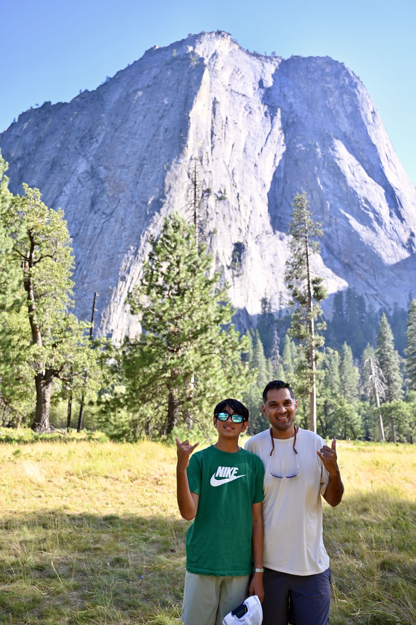 Our son and his dad in a grassy meadow, with the sheer granite face of El Capitan rising behind a line of pines.