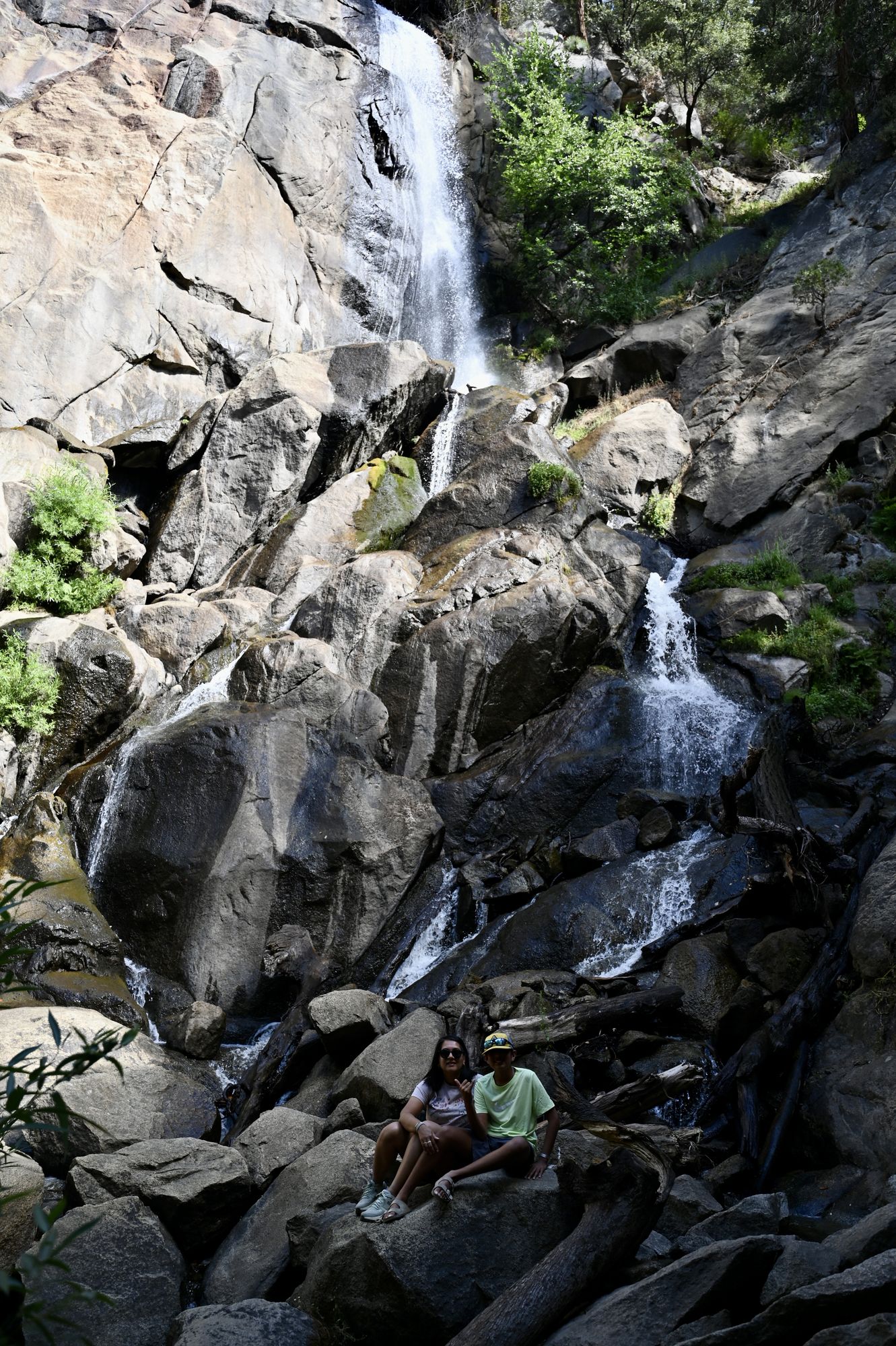 Grizzly falls cascading down a tall granite face into a pile of boulders, with two of us sitting at the bottom.