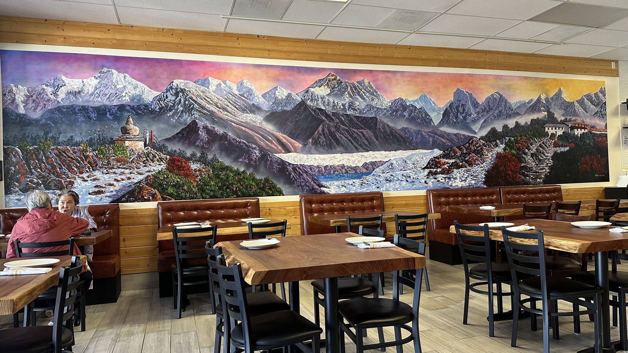 A restaurant dining room with a long mural of snowy Himalayan peaks and a stupa above the booths.