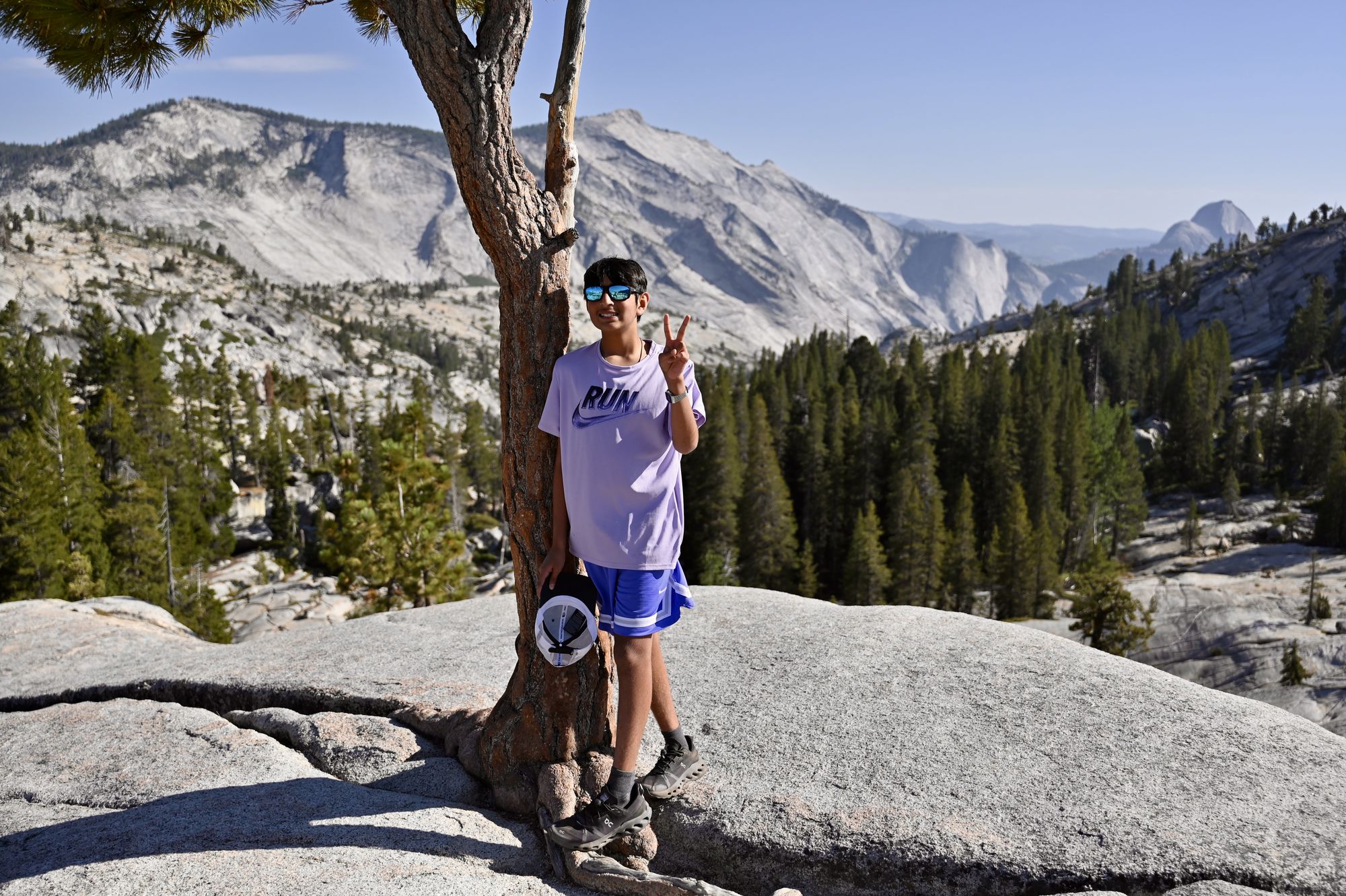 Our son standing under a small pine on smooth granite at Olmsted Point, with Half Dome on the horizon.