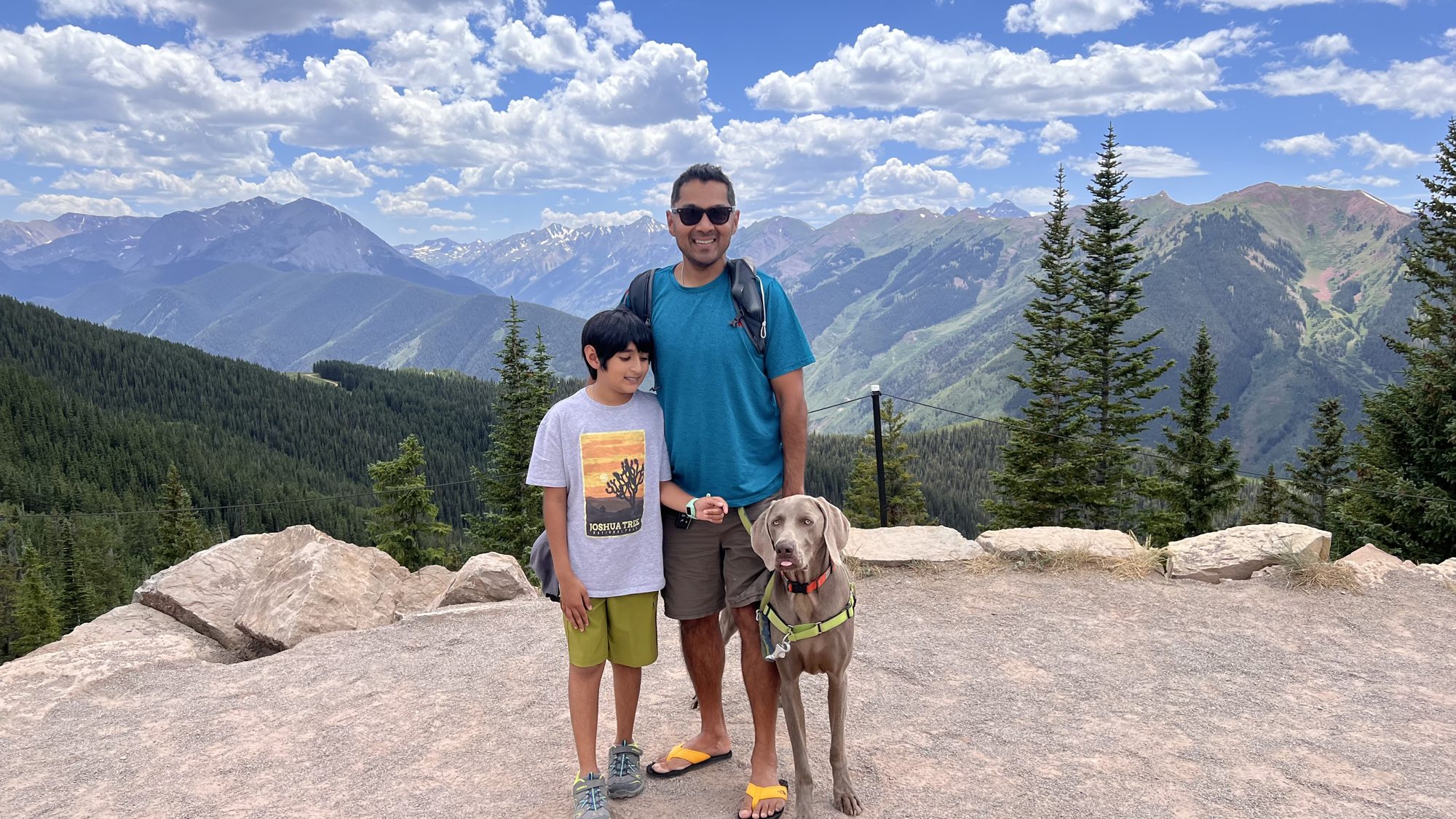 Man, boy and dog at the top of Aspen Mountain, with a range of peaks behind them