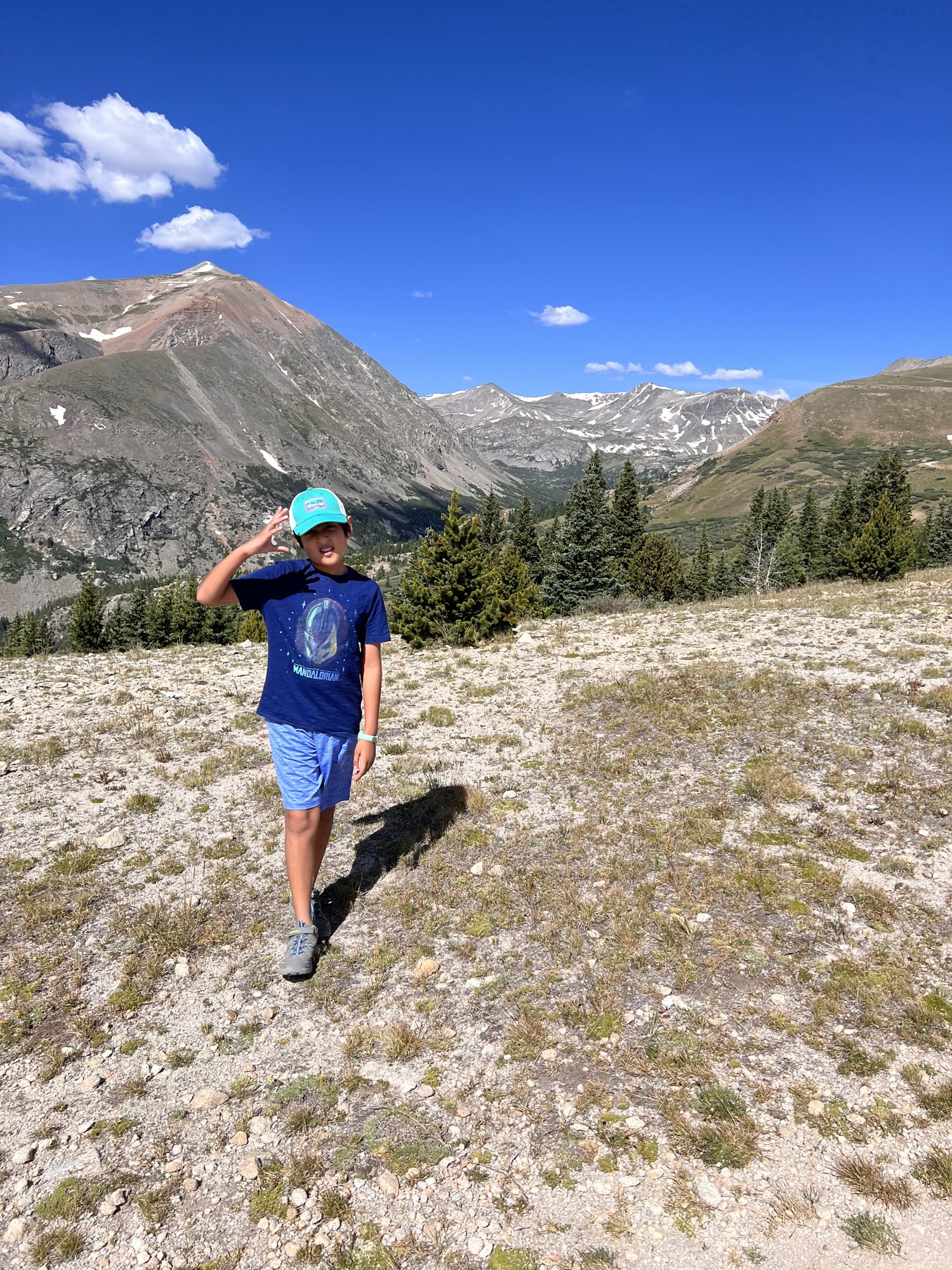 Boy standing on a high, open ridge with mountains and blue sky behind him