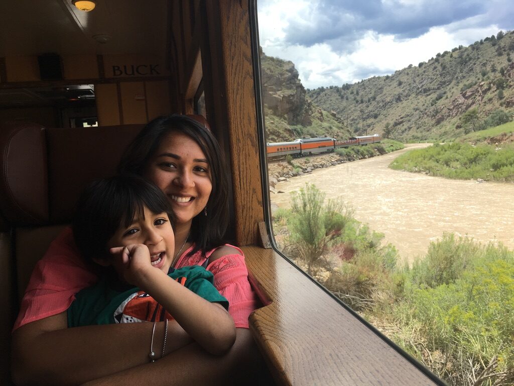 Woman and boy smiling by a train window, with the river and canyon outside
