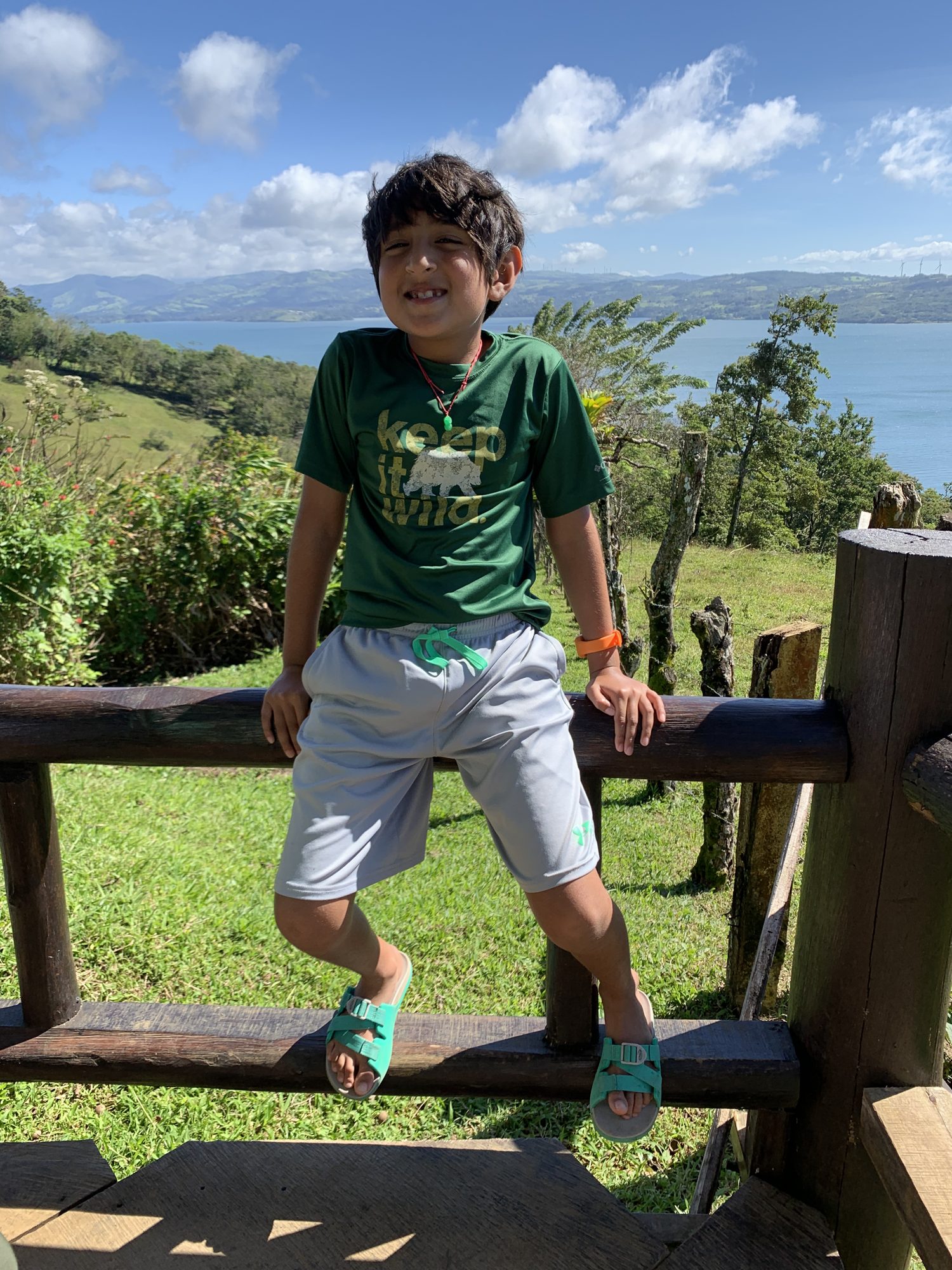Boy sitting on a fence at Café Macadamia, with Lake Arenal behind