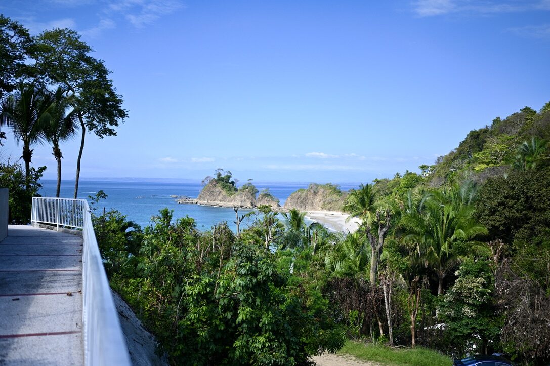 A coastal view of the bay and green headlands from a walkway above the beach