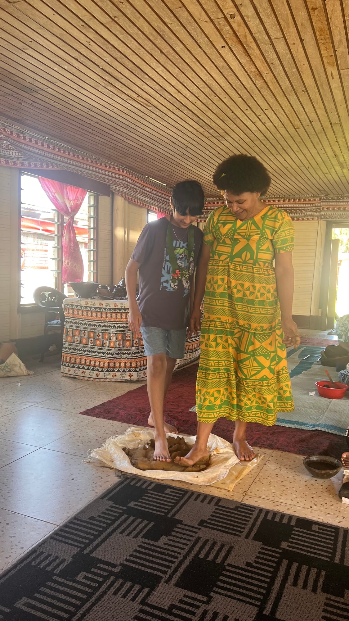 Our son and a village woman standing barefoot together on a mound of wet clay on a cloth, working it with their feet.