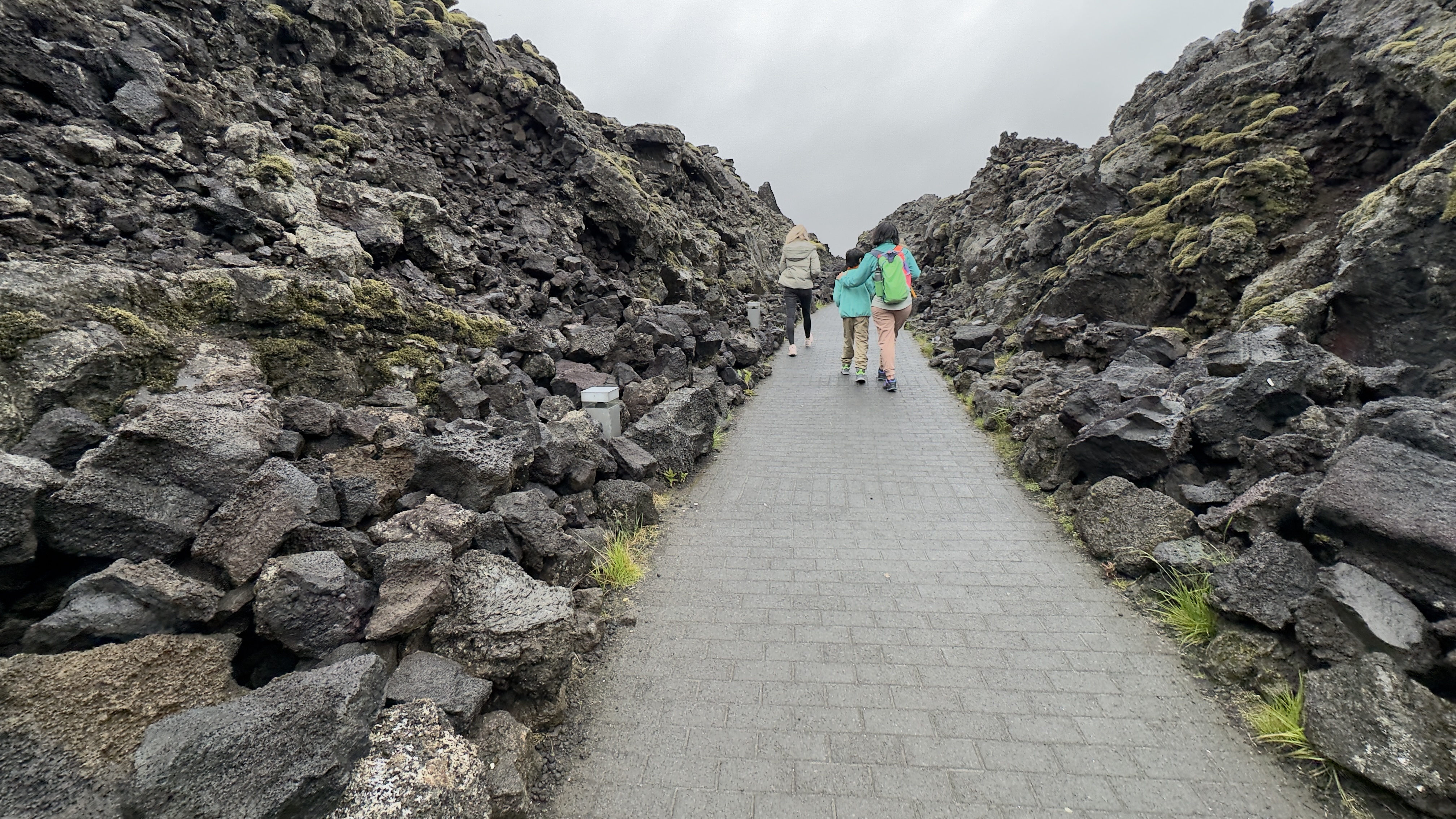 Woman and child walking on a path covered on both sides with 10 feet of volcanic rock formations.
