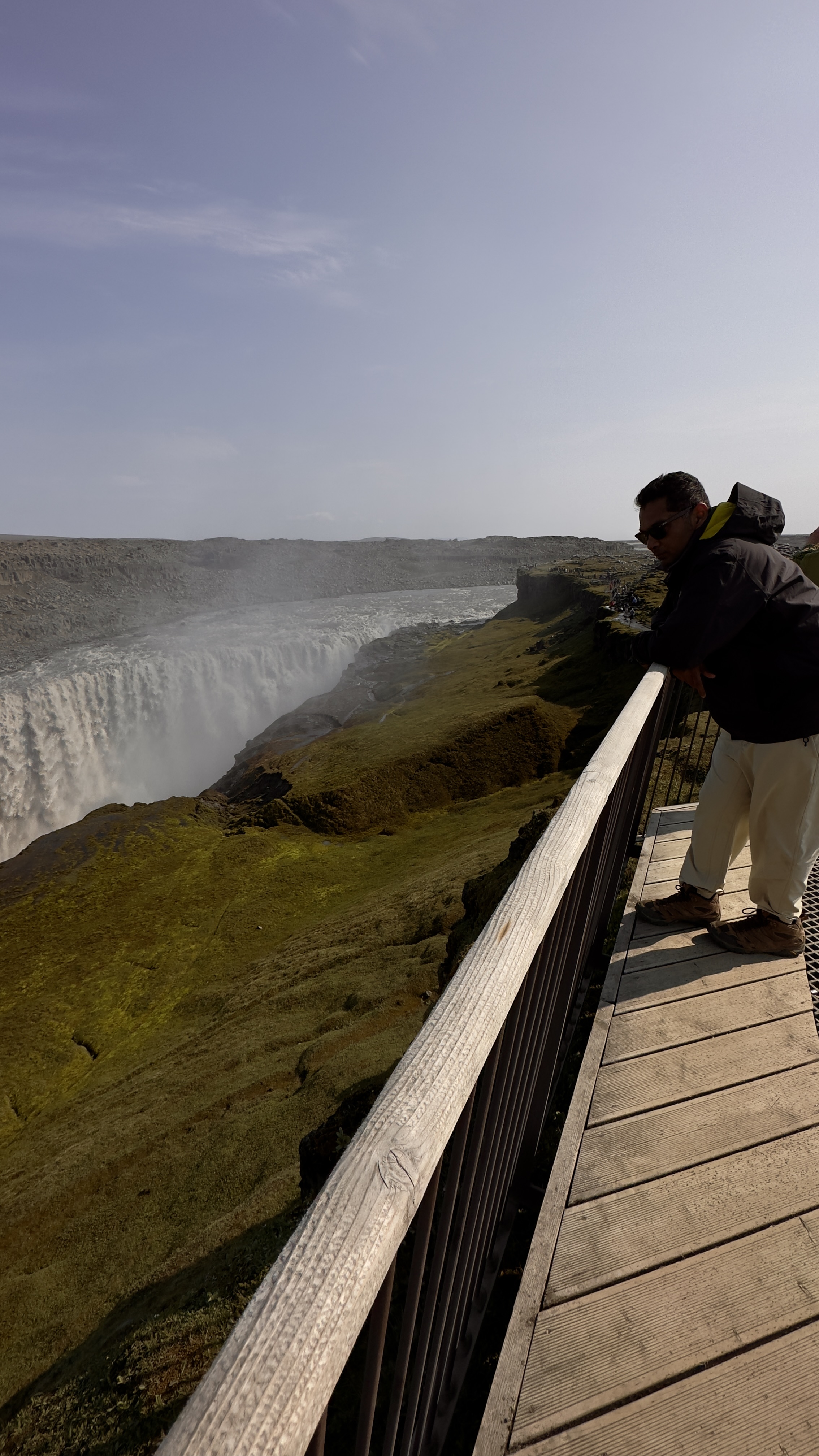 A man looking at a waterfall named Dettifoss from the viewing deck and the hills are covered with moss