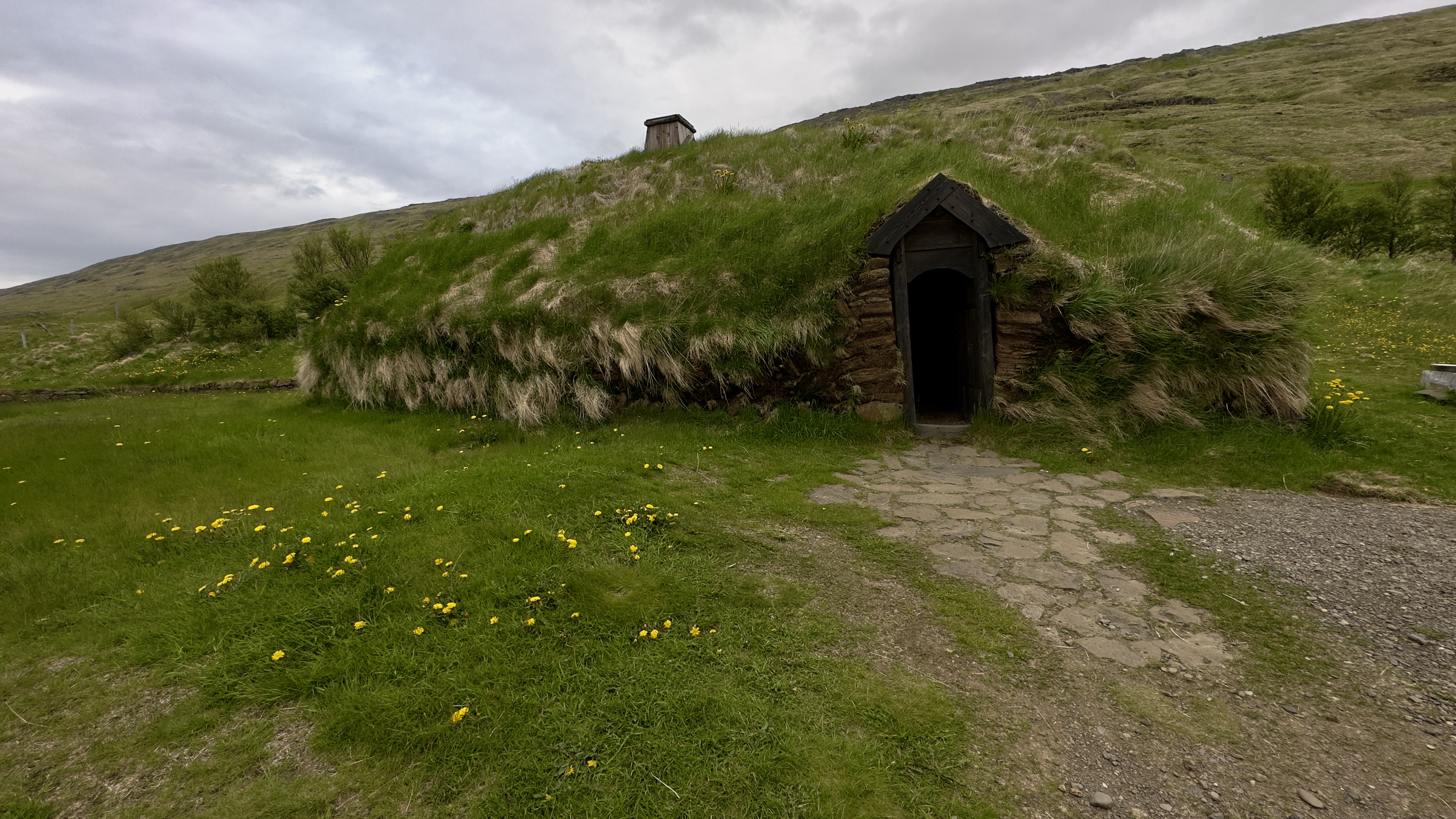 Eirikstadir Viking Longhouse museum is a turf covered wooden house with a small door and hillside behind it.