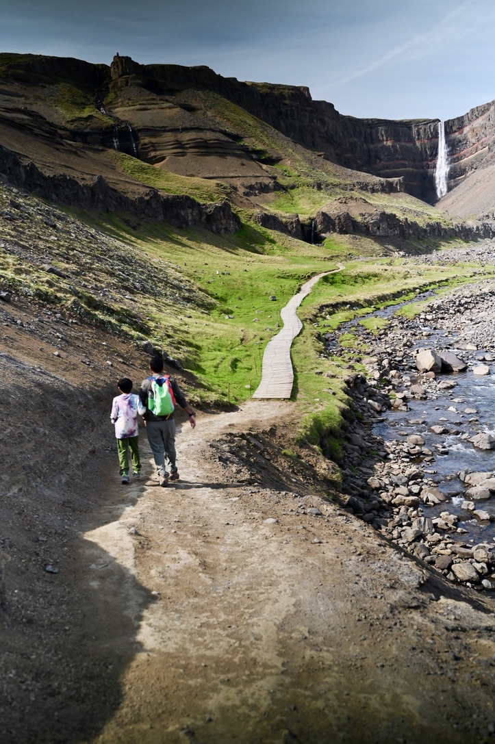 Man and kid walking on board walk towards a waterfall named Hengifoss