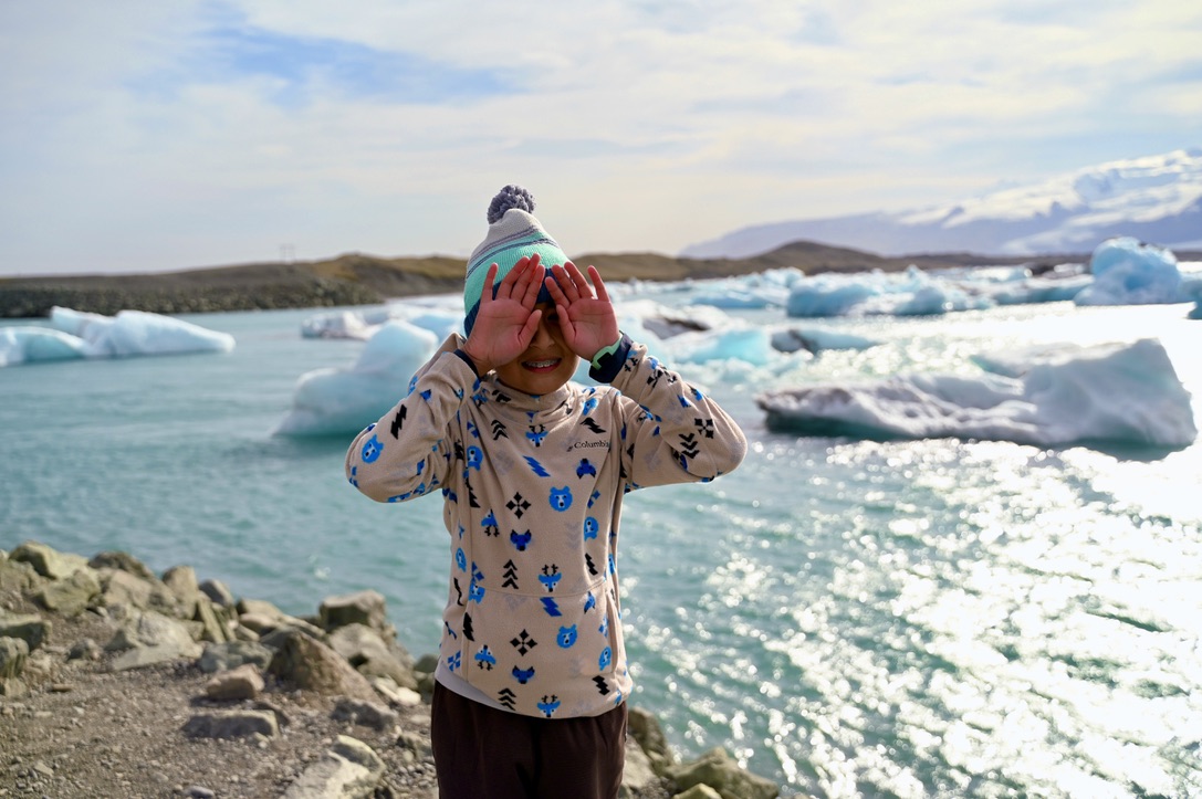 Kid standing with palms on eyes in front of a glacier lagoon