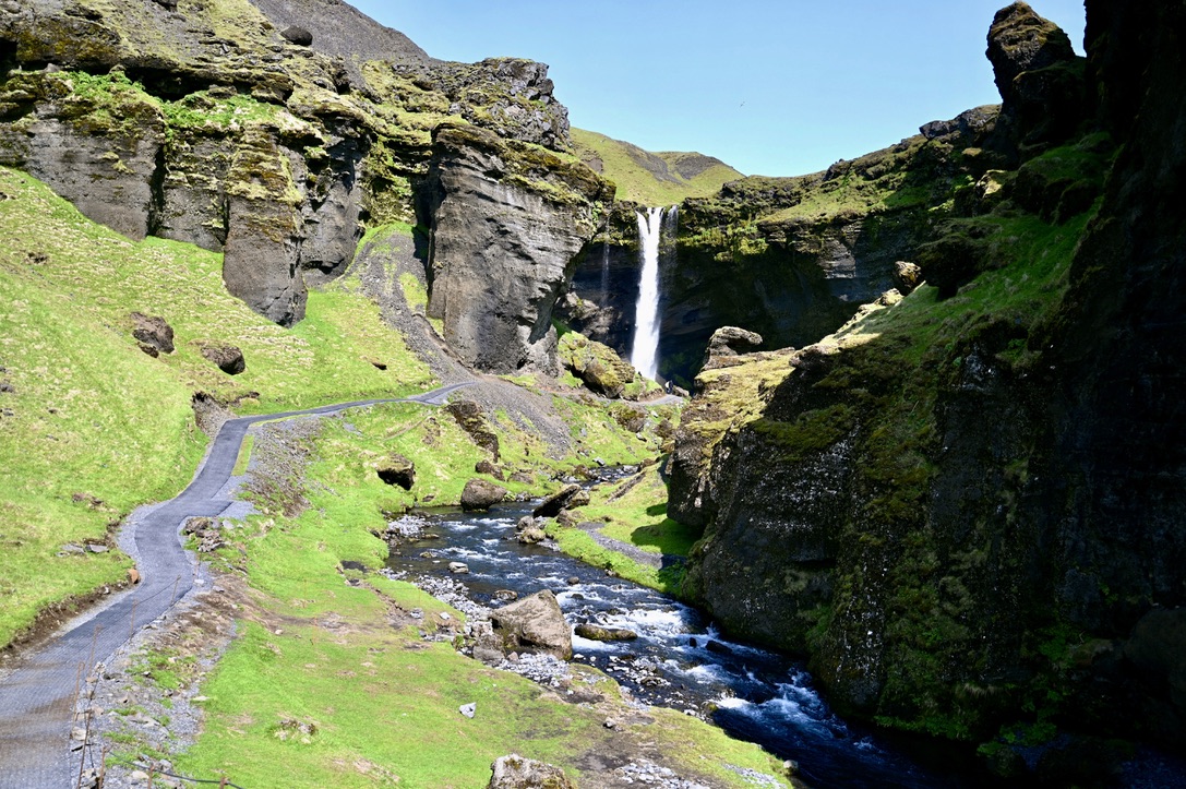 Kvernufoss waterfall in Iceland, with leading pathway and river, sided by moss covered hills