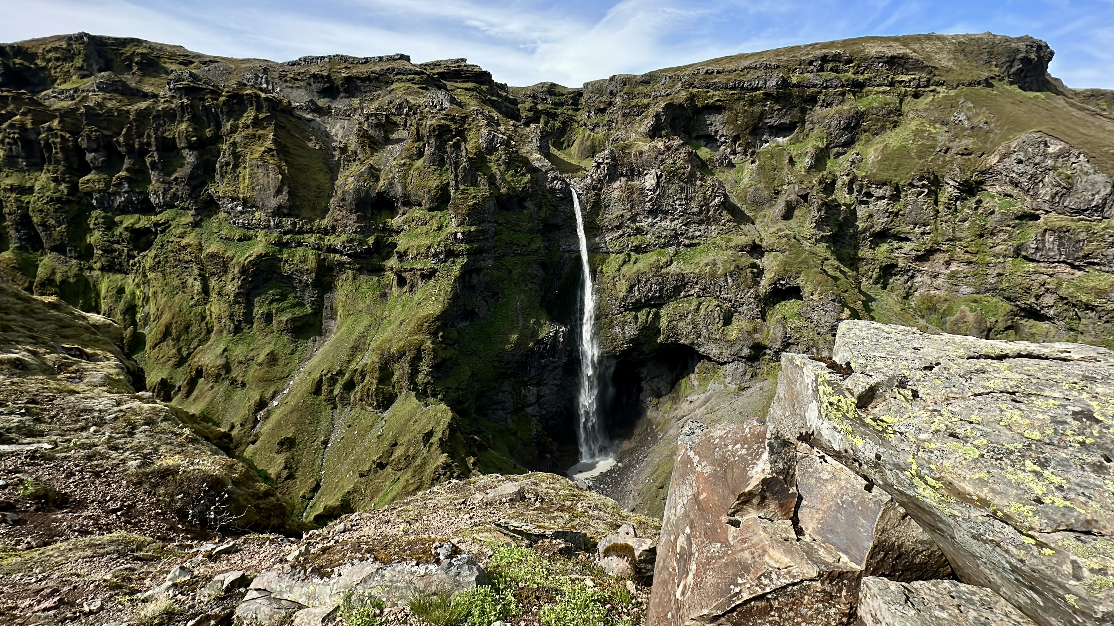 Tall waterfall coming down a mountain side covered with lush moss and canyon rocks in the foreground.