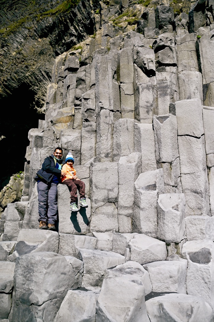 Father and son sitting on basalt columns of hill face at Reynisfjara beach
