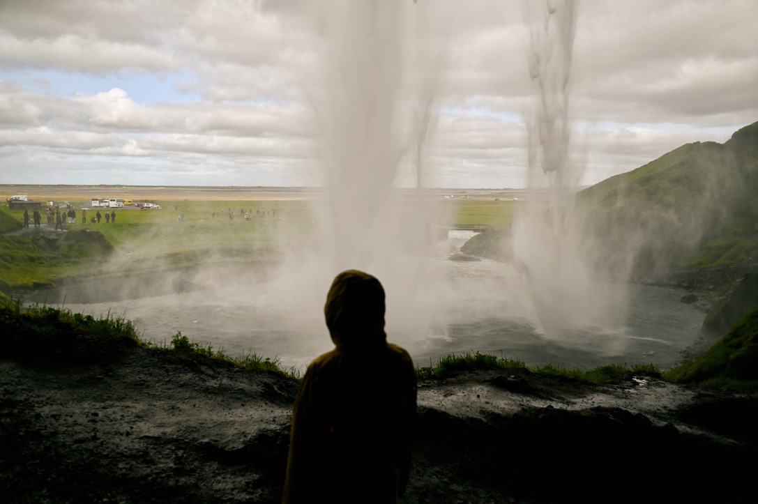 Boy standing behind the Seljalandsfoss waterfall in Iceland