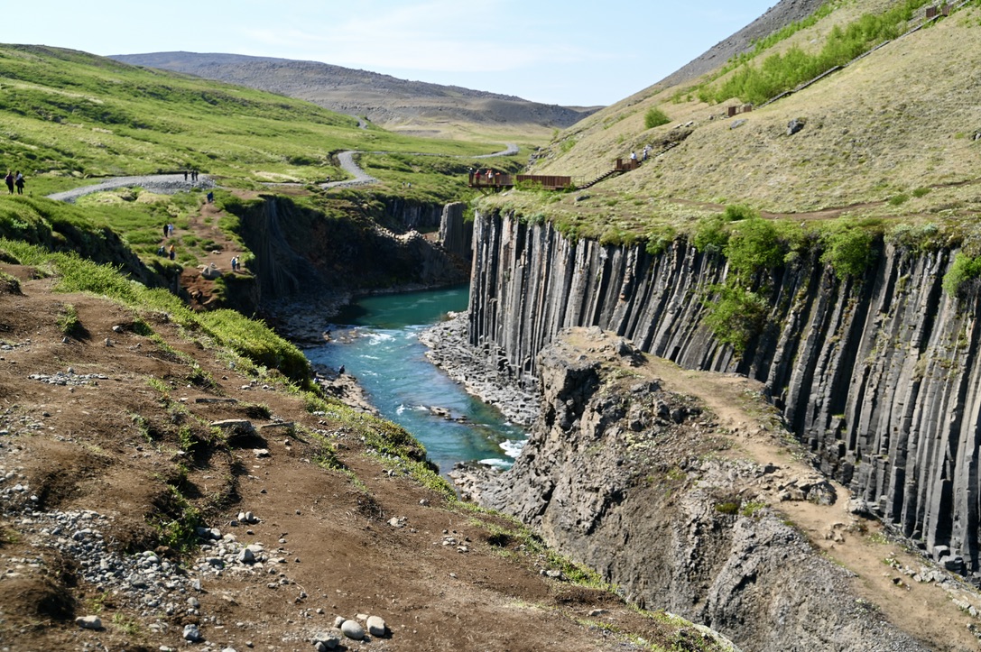 A canyon with river flowing through it with basalt columns and moss covered hills