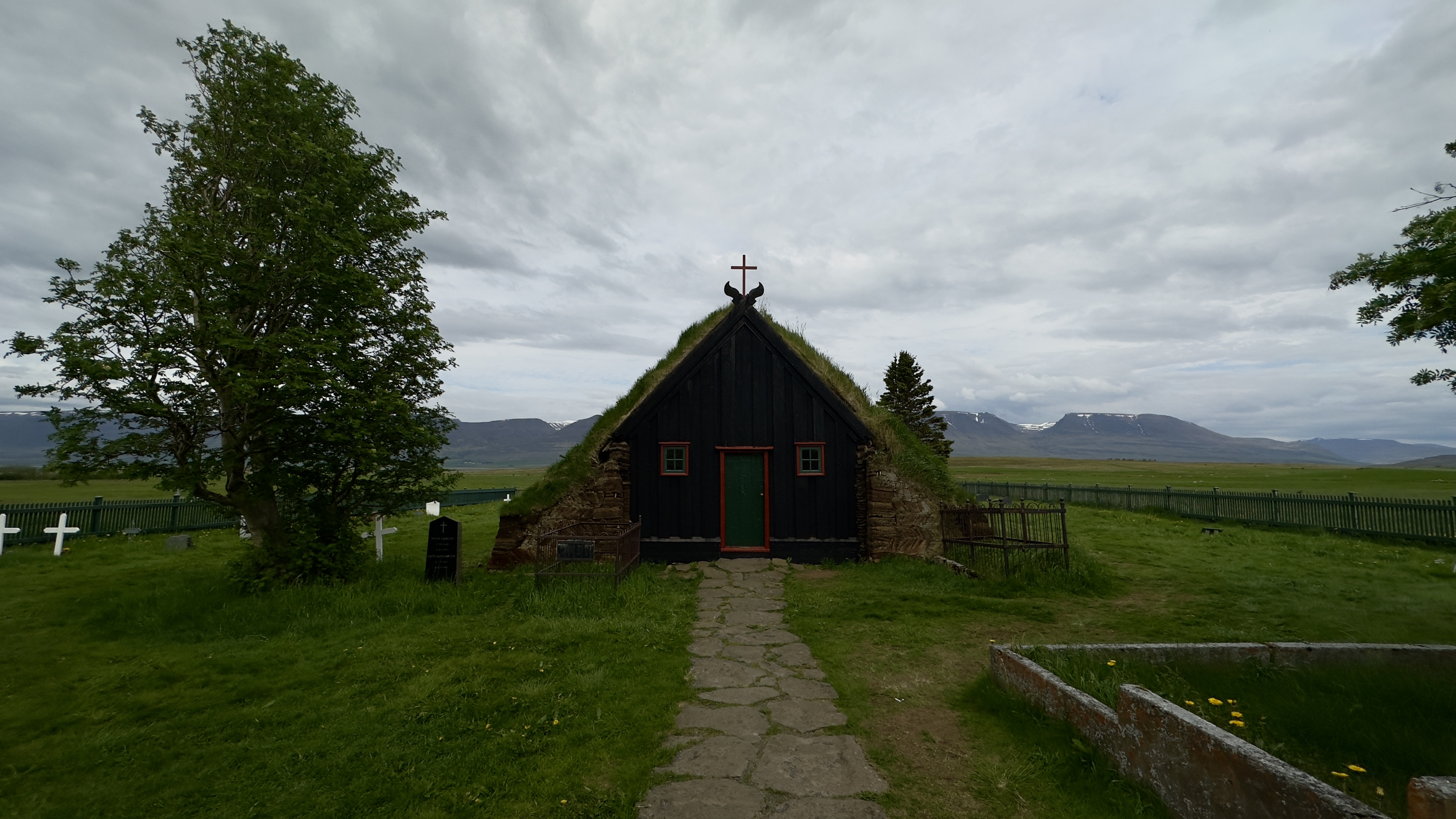 Wooden church with turf on roof and pathway leading to it, with mountains in the background