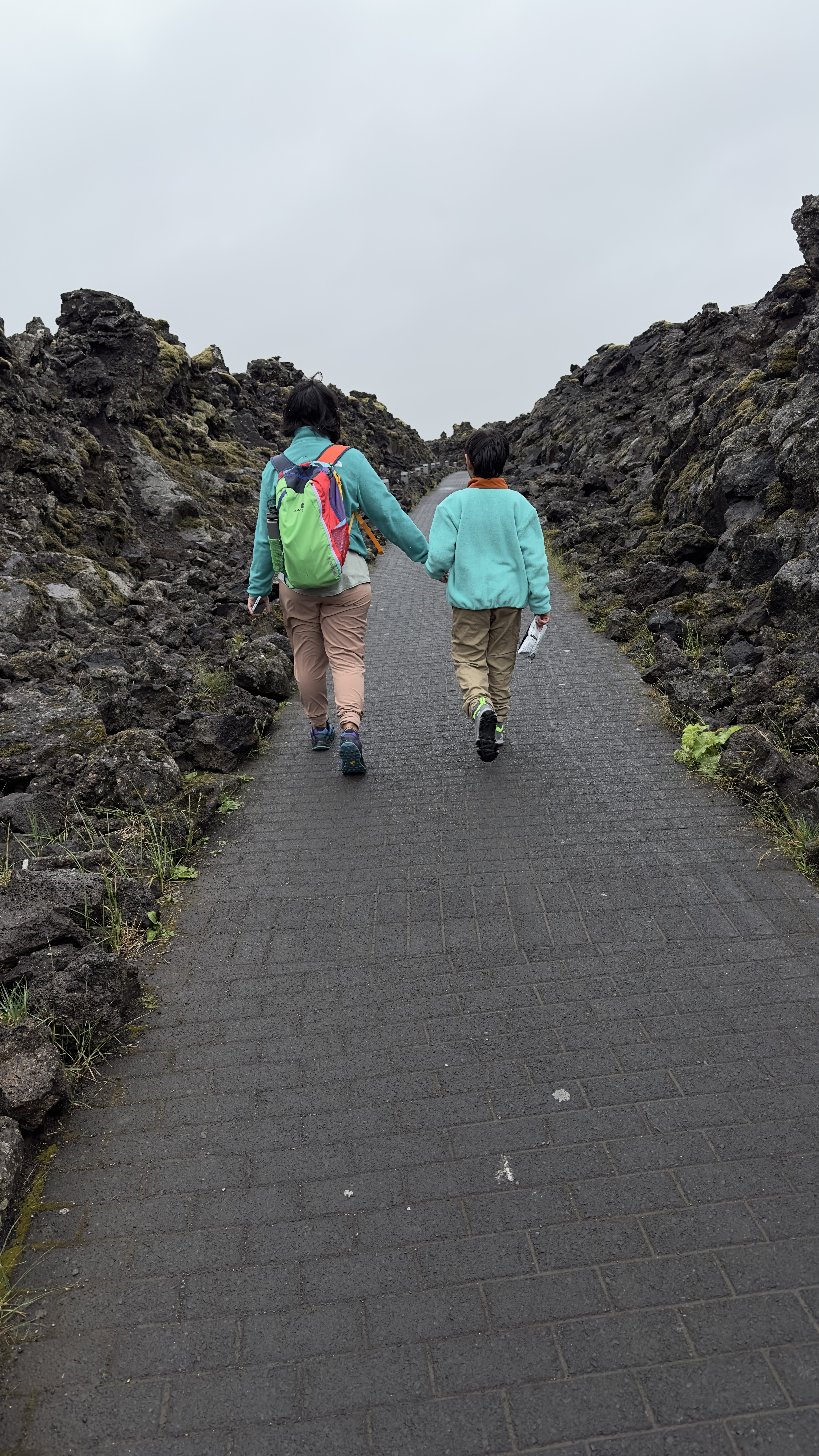 Mother and son walking on path surrounded by volcanic rock in Blue Lagoon, Iceland
