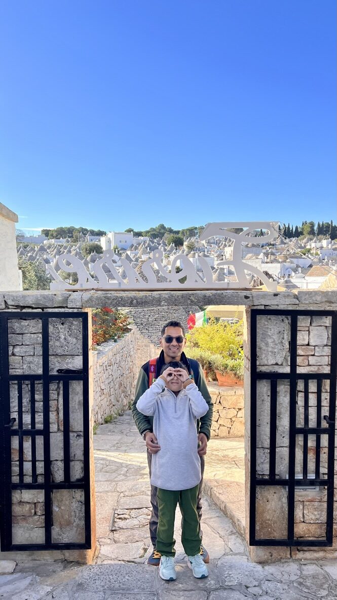 Man and boy at a gate in a stone wall, with the trulli rooftops behind
