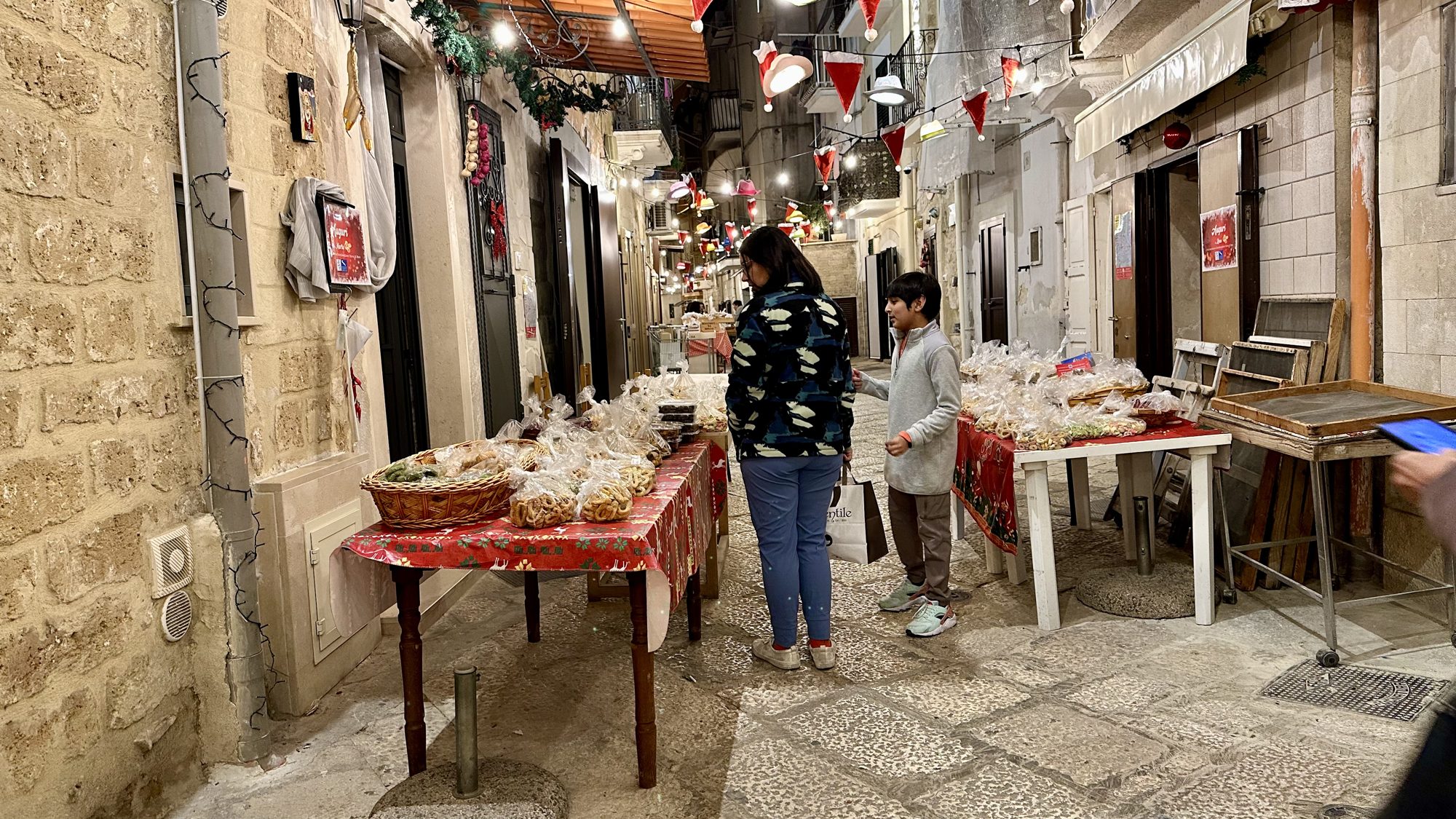 Tables of drying handmade pasta along a narrow street, with a woman and boy browsing