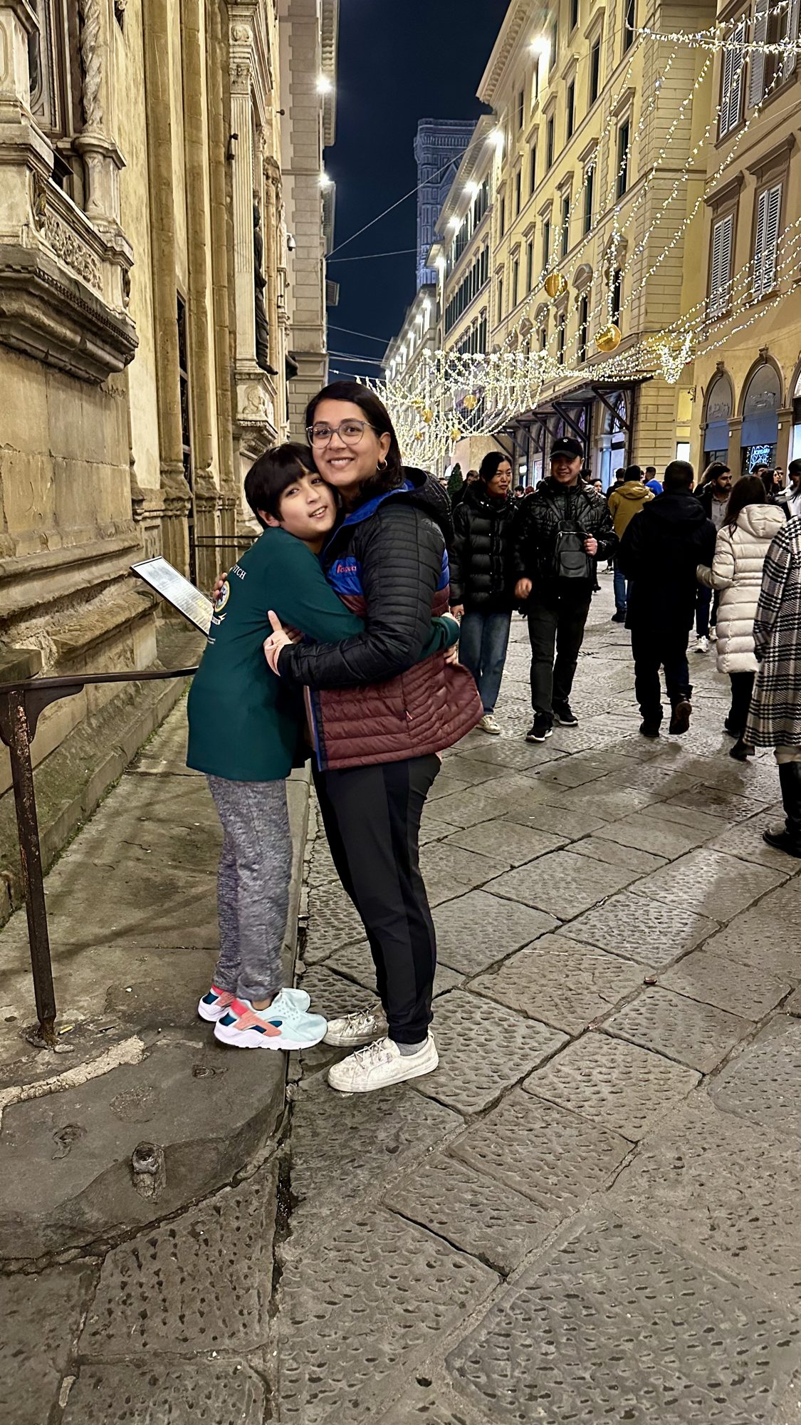 Woman and boy hugging on a crowded, lit-up street in Florence at night