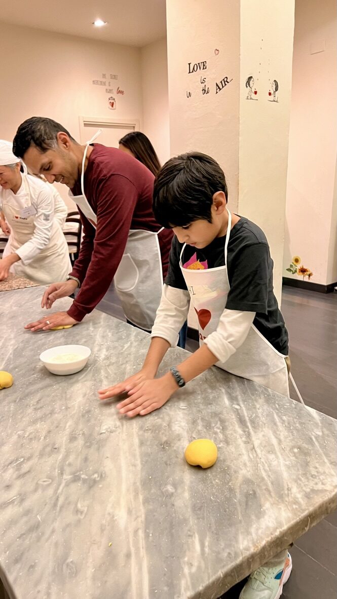 Boy and man kneading pasta dough at a marble counter in aprons