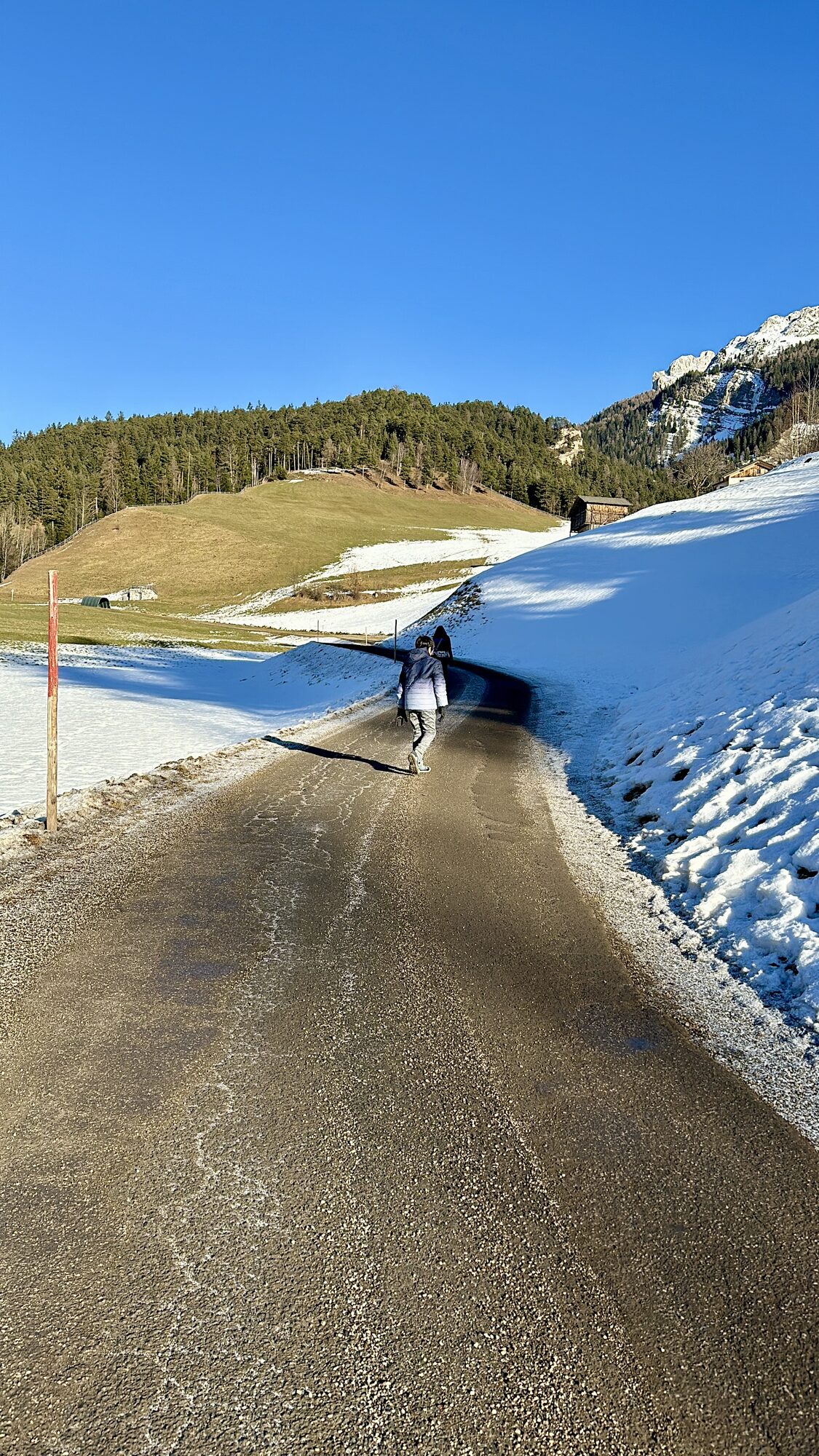 A narrow road with snow banks leading out of the village toward the hills
