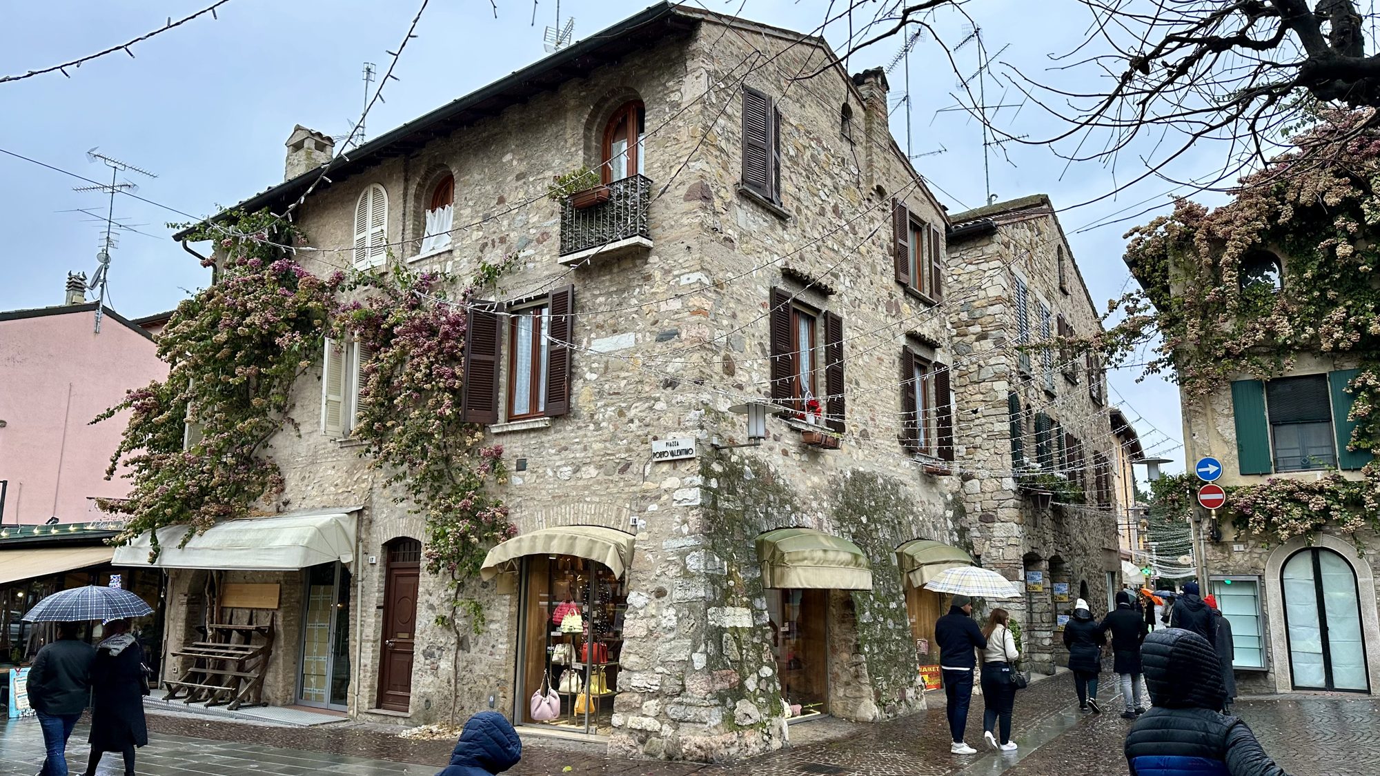 A stone building covered in climbing plants on a street in Sirmione
