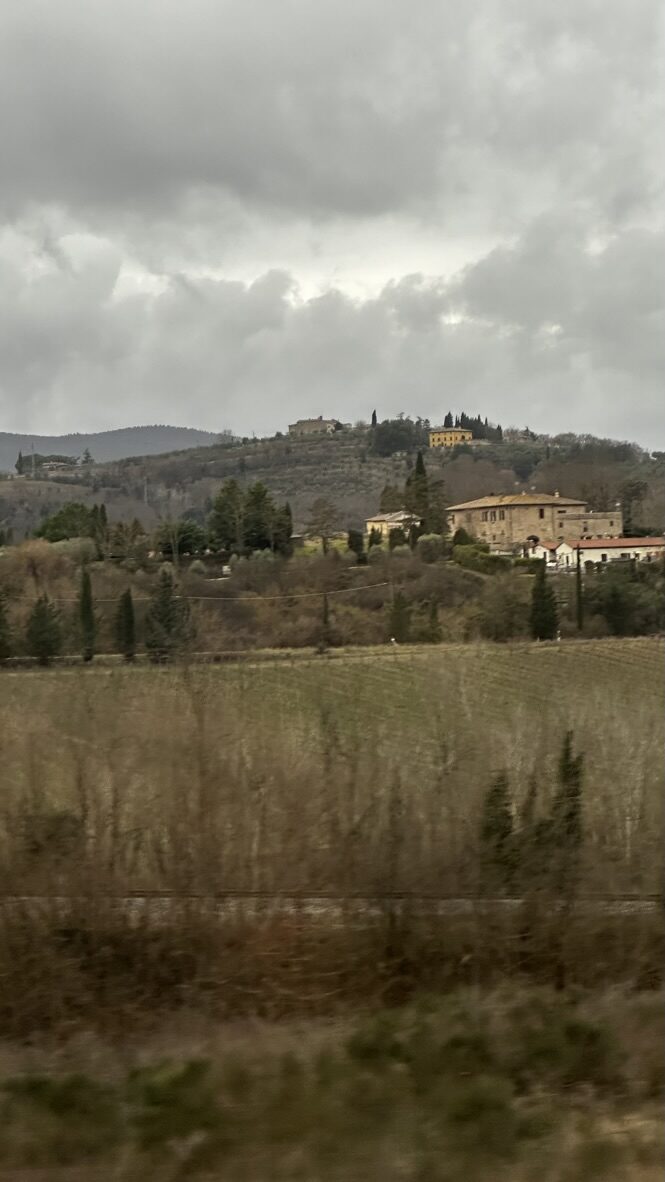 Tuscan fields and a hilltop farmhouse under a cloudy sky
