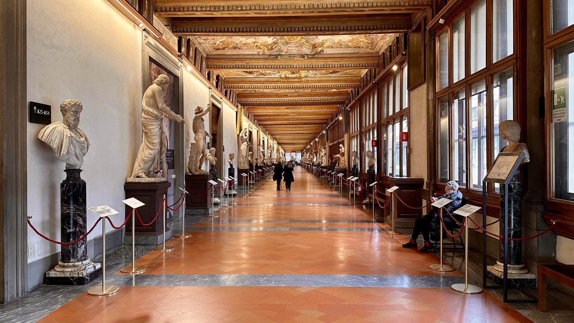 A long gallery hallway lined with statues under a painted ceiling