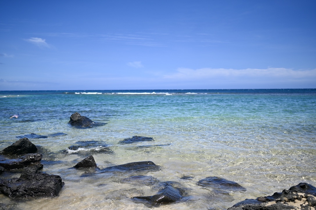 _Blue green ocean by a sandy beach with big rocks.