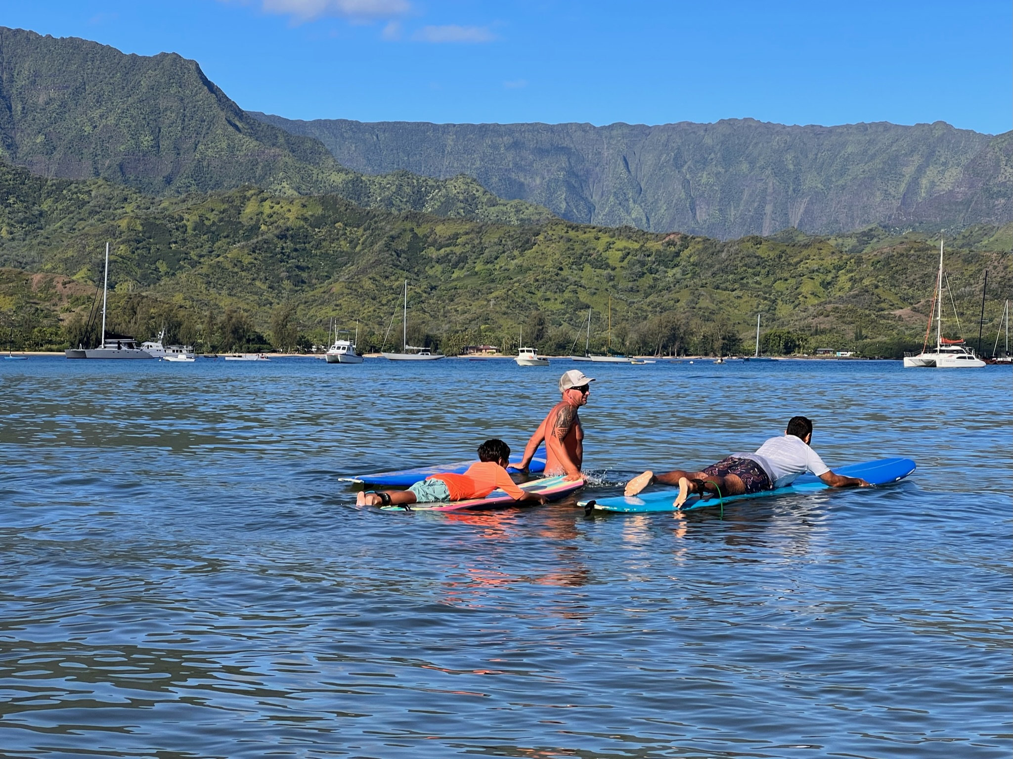 Boy and man learning to surf lying flat on surf board with instructor in the middle at Hanalei bay.