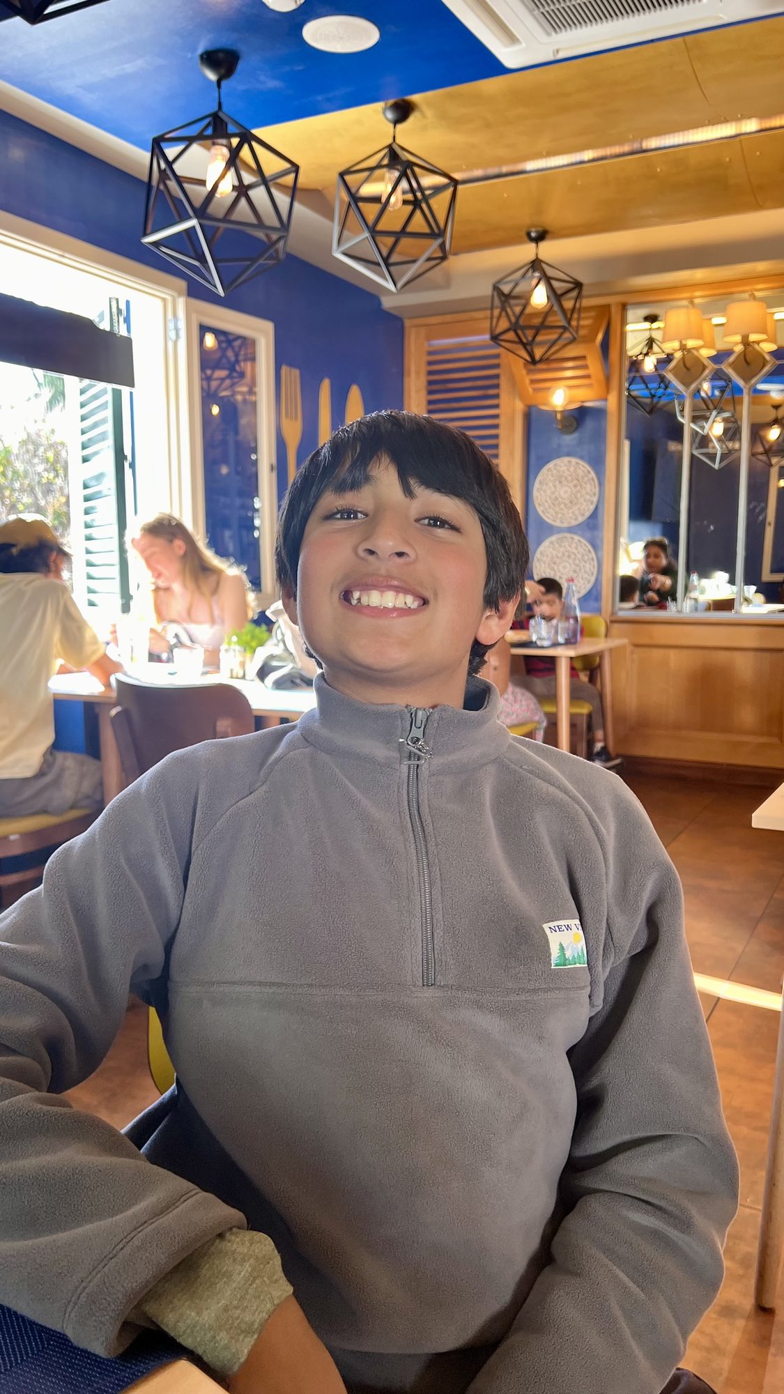Our son grinning at the table inside the restaurant, with blue walls and geometric pendant lights.