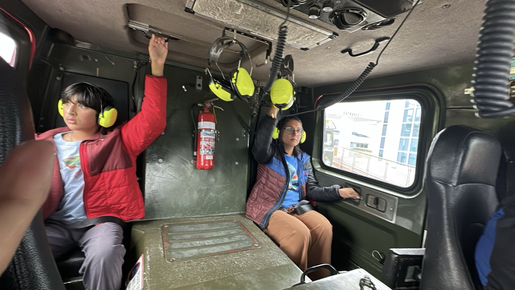 Our son and I wearing yellow ear defenders inside the cabin of the Hägglund vehicle.