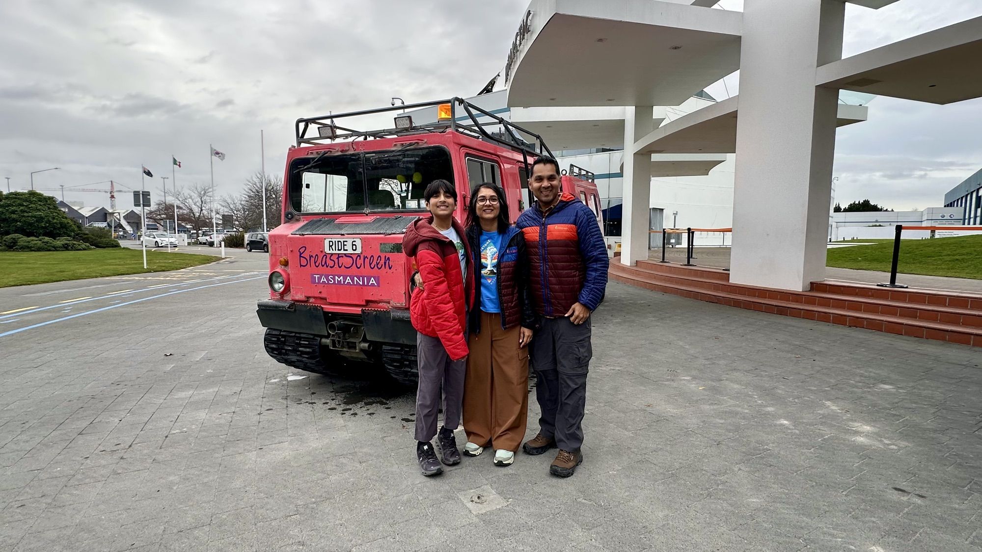 The three of us standing in front of the red Hägglund all-terrain vehicle outside the centre.