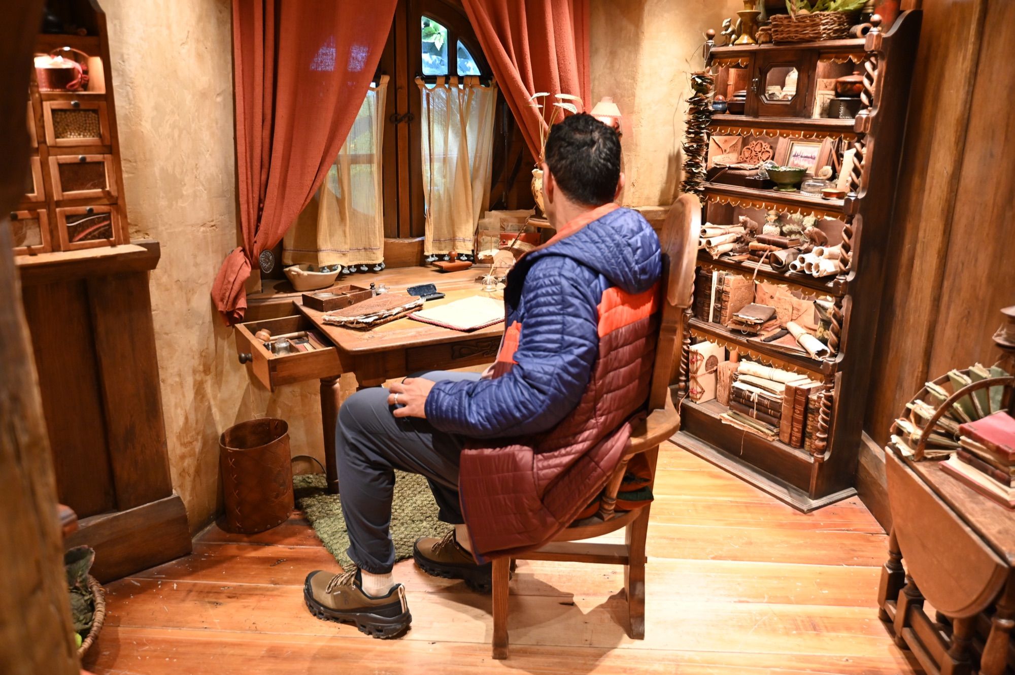 His dad sitting at a writing desk inside a hobbit hole, surrounded by wooden shelves, books and red curtains.