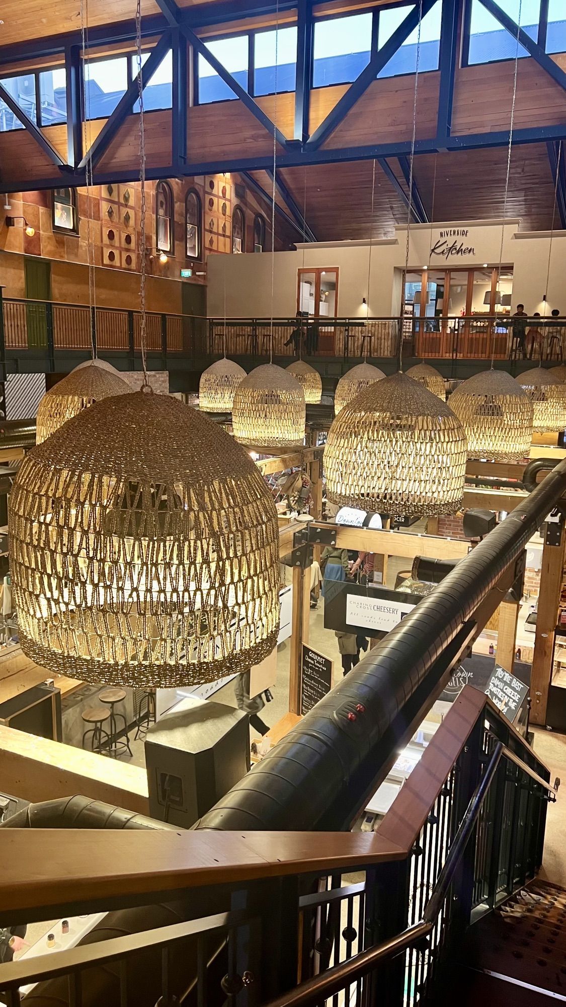 Looking down from an upper floor of Riverside Market at woven pendant lights and food stalls below.
