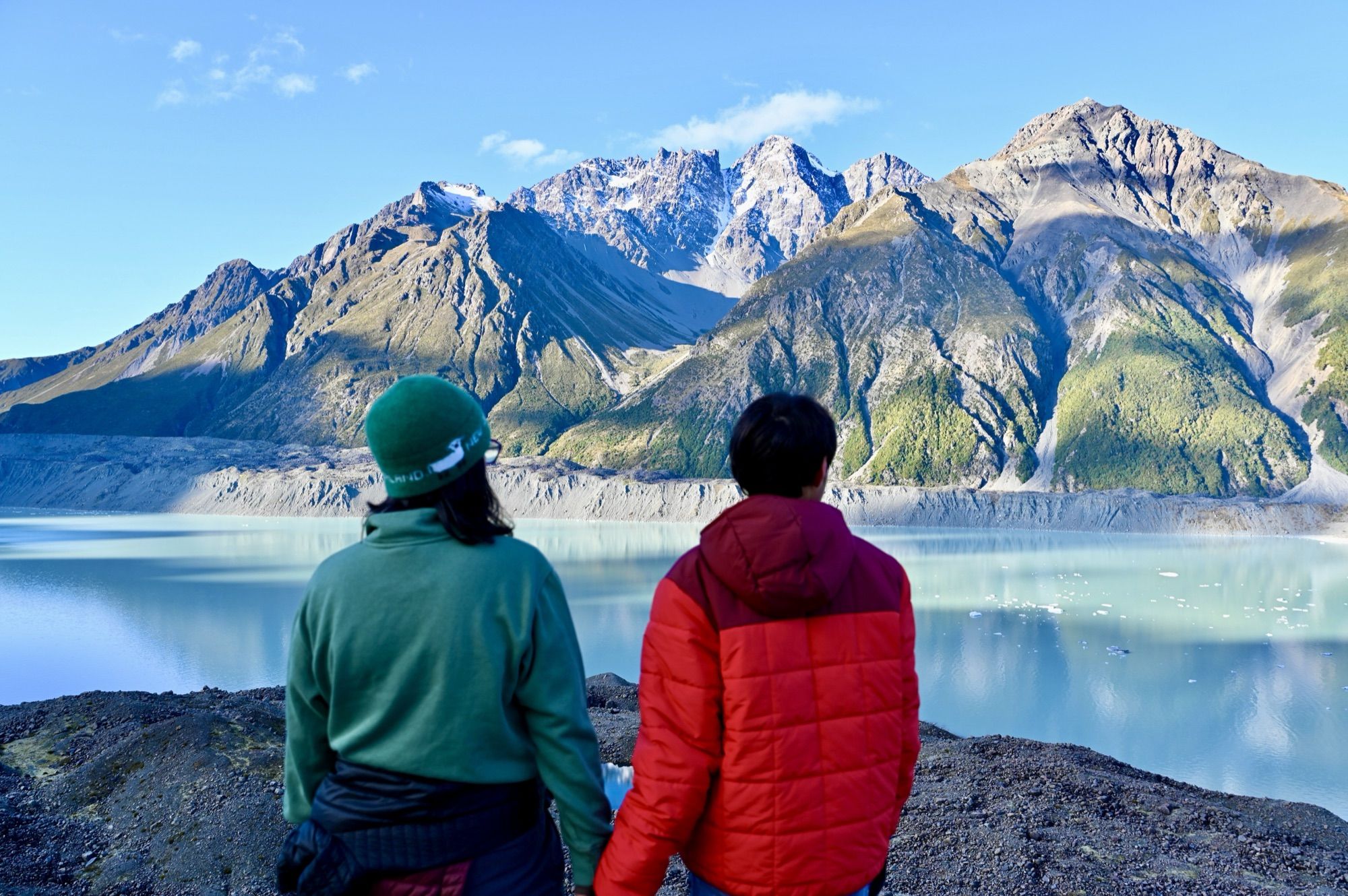 Me and our son from behind, looking out over the pale turquoise Tasman Glacier lake to the mountains.