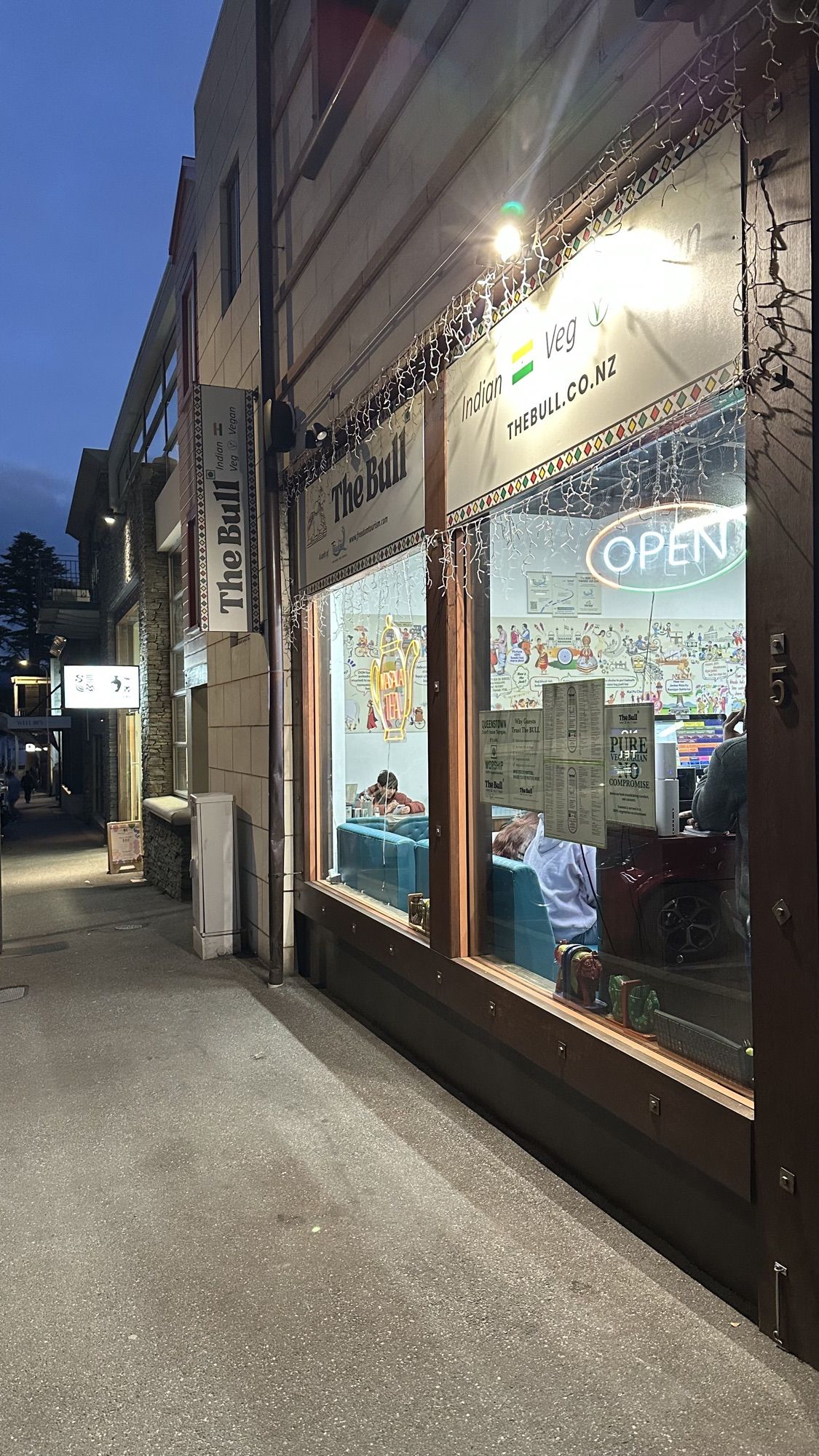 The lit-up front window of The Bull restaurant on a quiet street at dusk, with an “Open” sign.