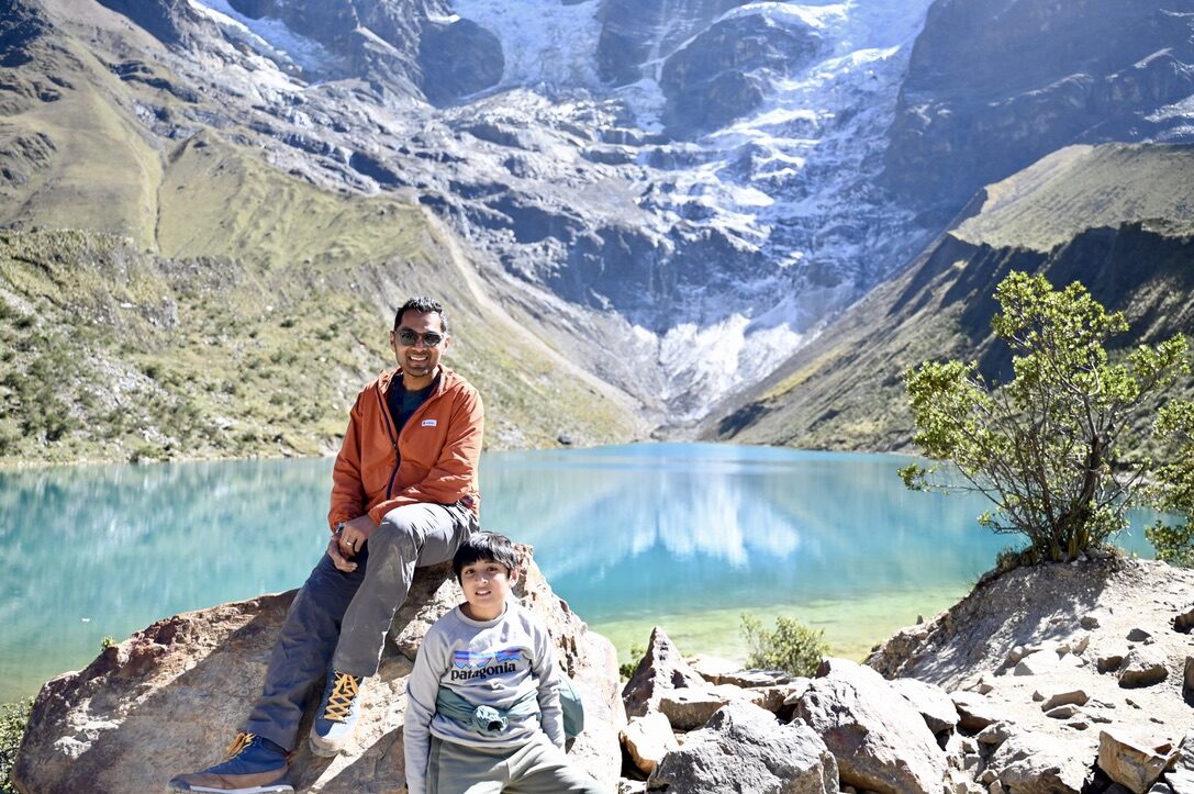 Man and boy sitting on rocks above the turquoise Humantay Lake below the glacier