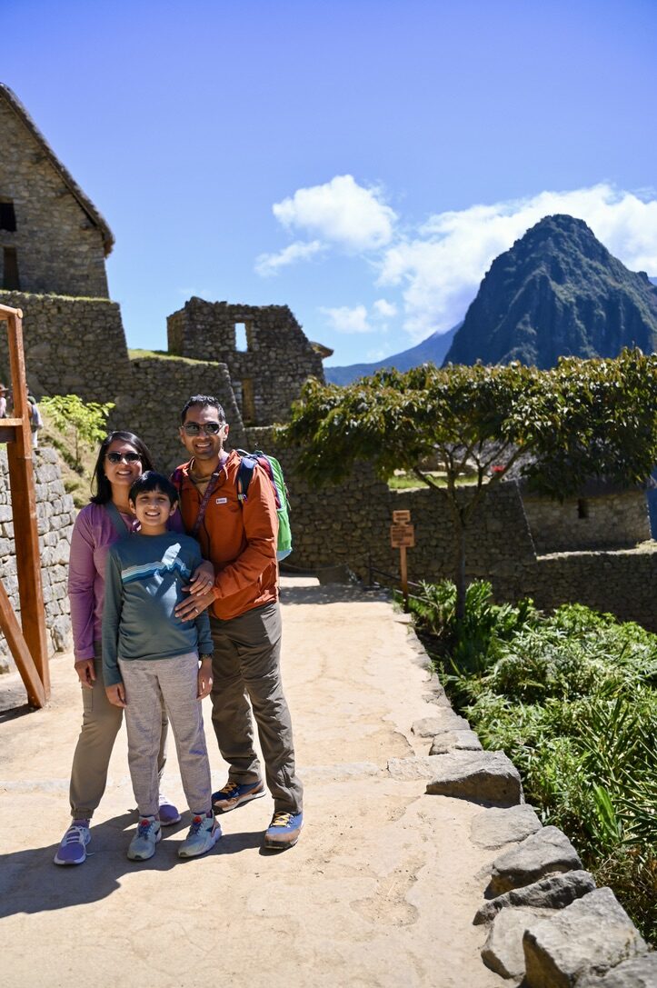 Woman, boy and man smiling on a stone path, with Huayna Picchu behind