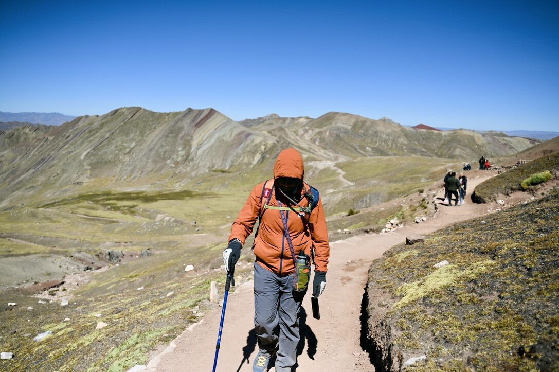 Man in an orange jacket hiking with poles along the trail into the colorful valley