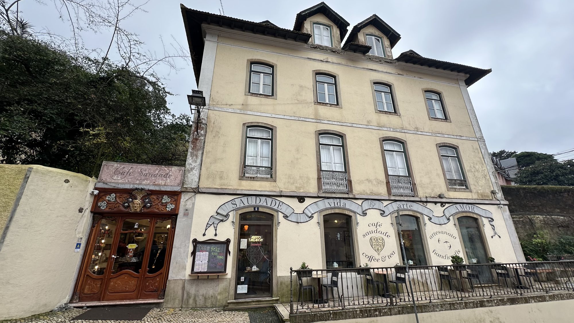 The cream-colored building of Café Saudade in Sintra, with its ornate wooden door and terrace.