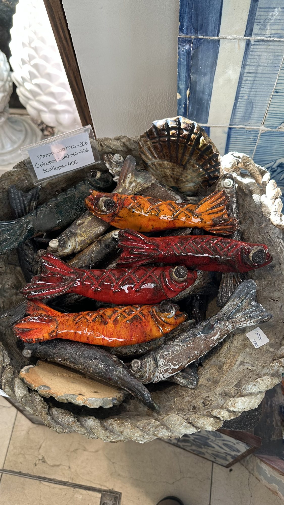 A basket of glazed ceramic fish in red, orange and silver, for sale in a souvenir shop.