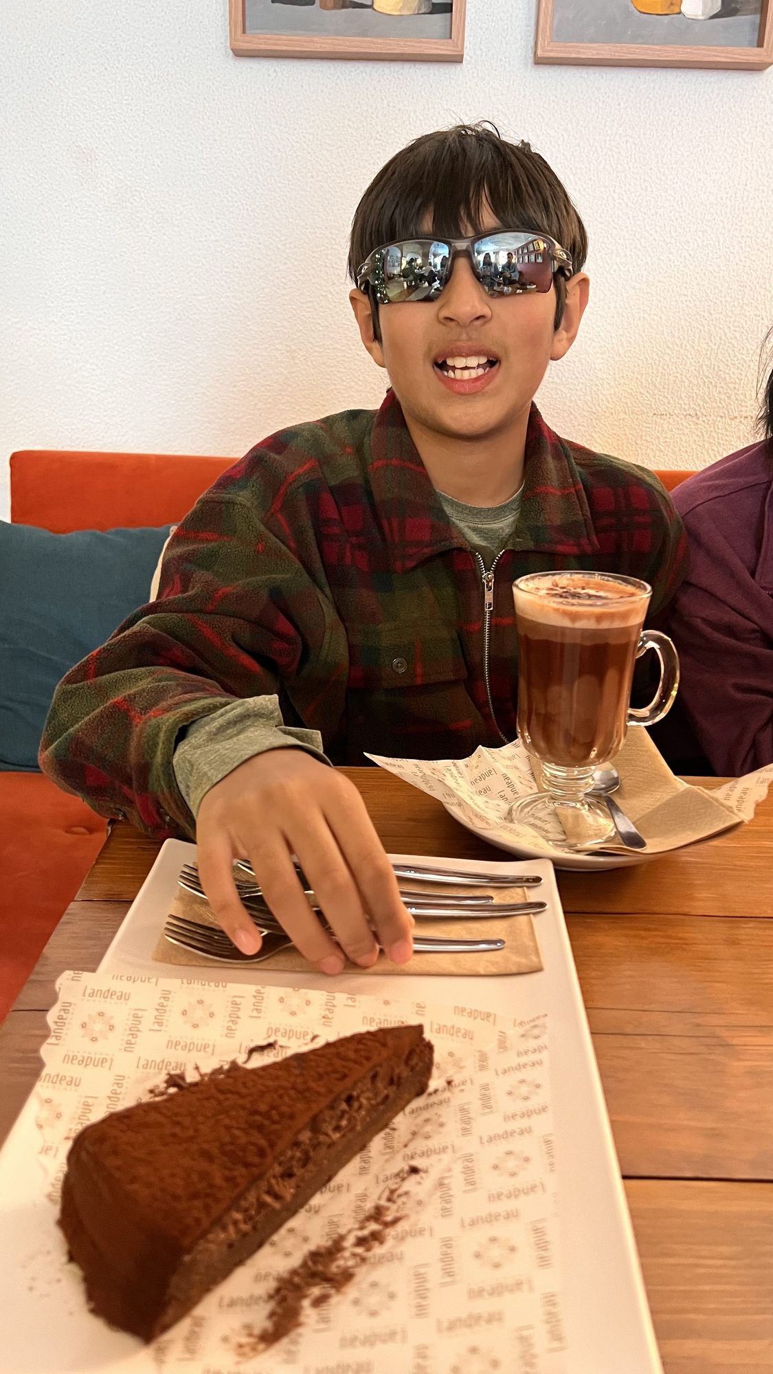 Our son grinning behind a slice of chocolate cake dusted with cocoa and a tall glass of hot chocolate.