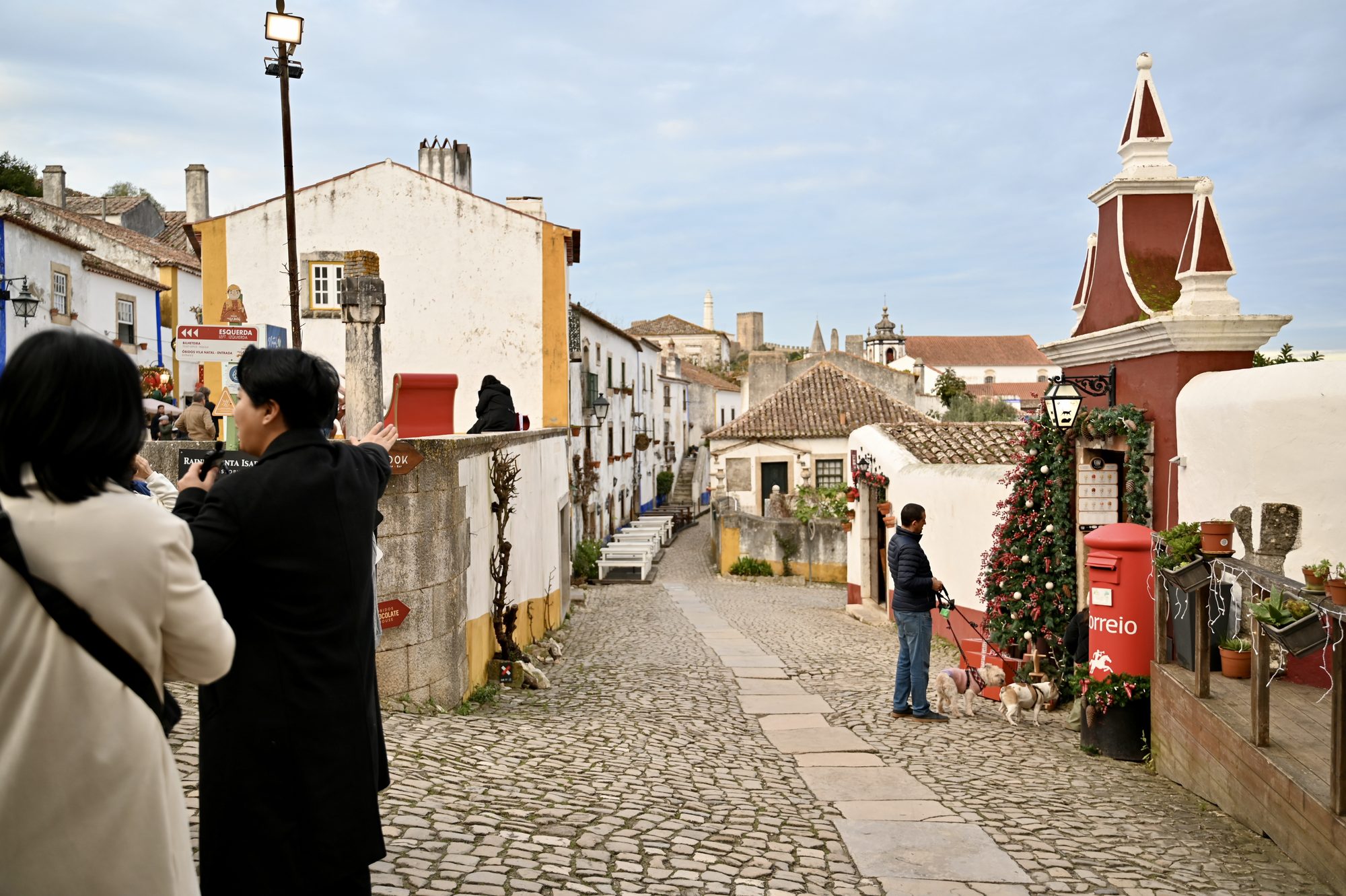 A cobbled street in Óbidos with whitewashed houses, a Christmas tree and a red post box.