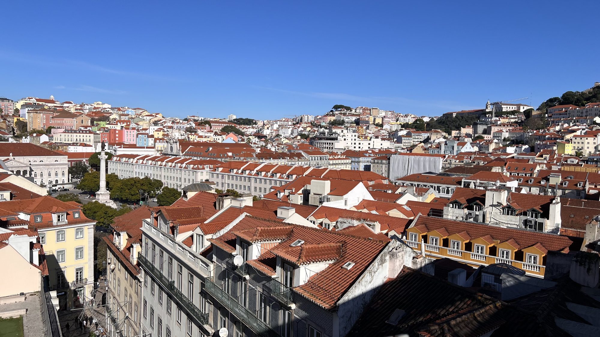 A wide view over the red rooftops of the Baixa towards the hills of Lisbon.