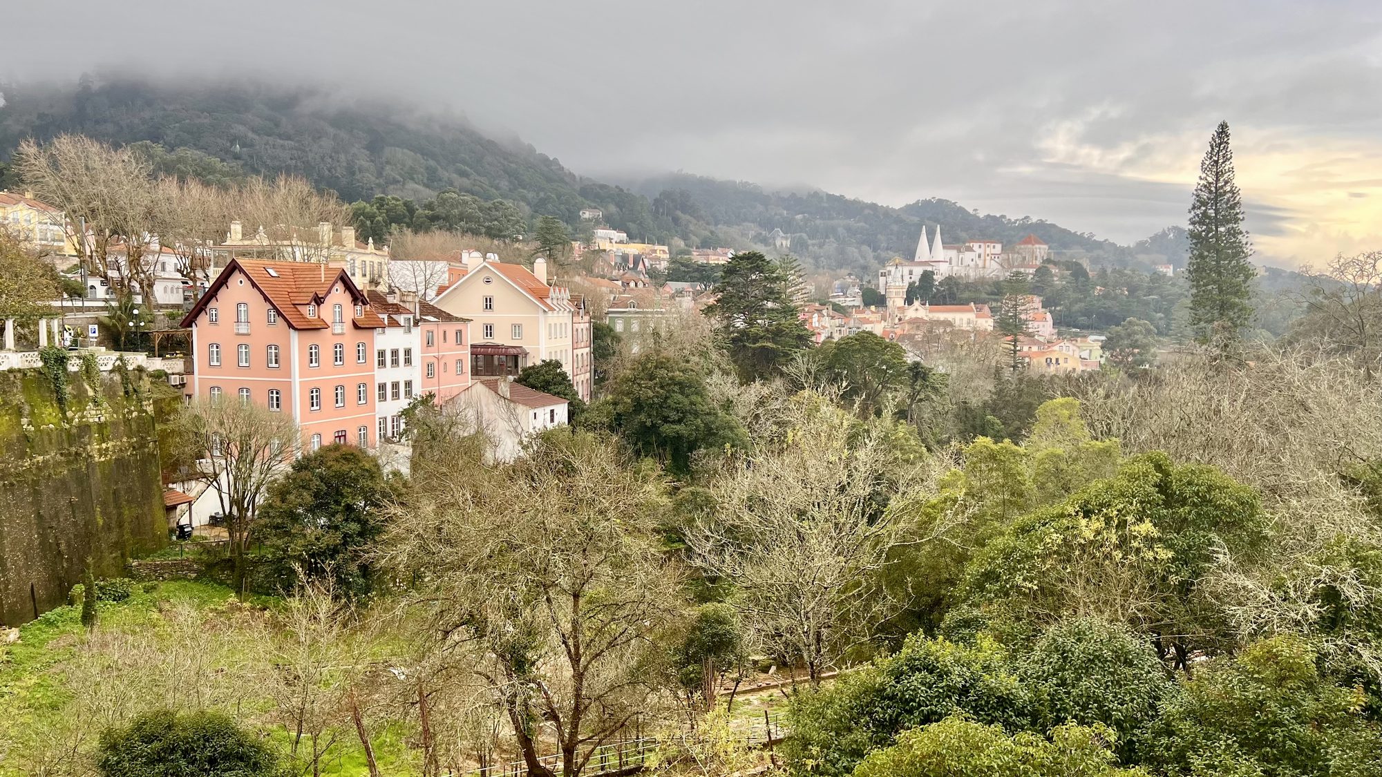 Pastel houses of Sintra among green trees, with mist hanging over the hills behind.